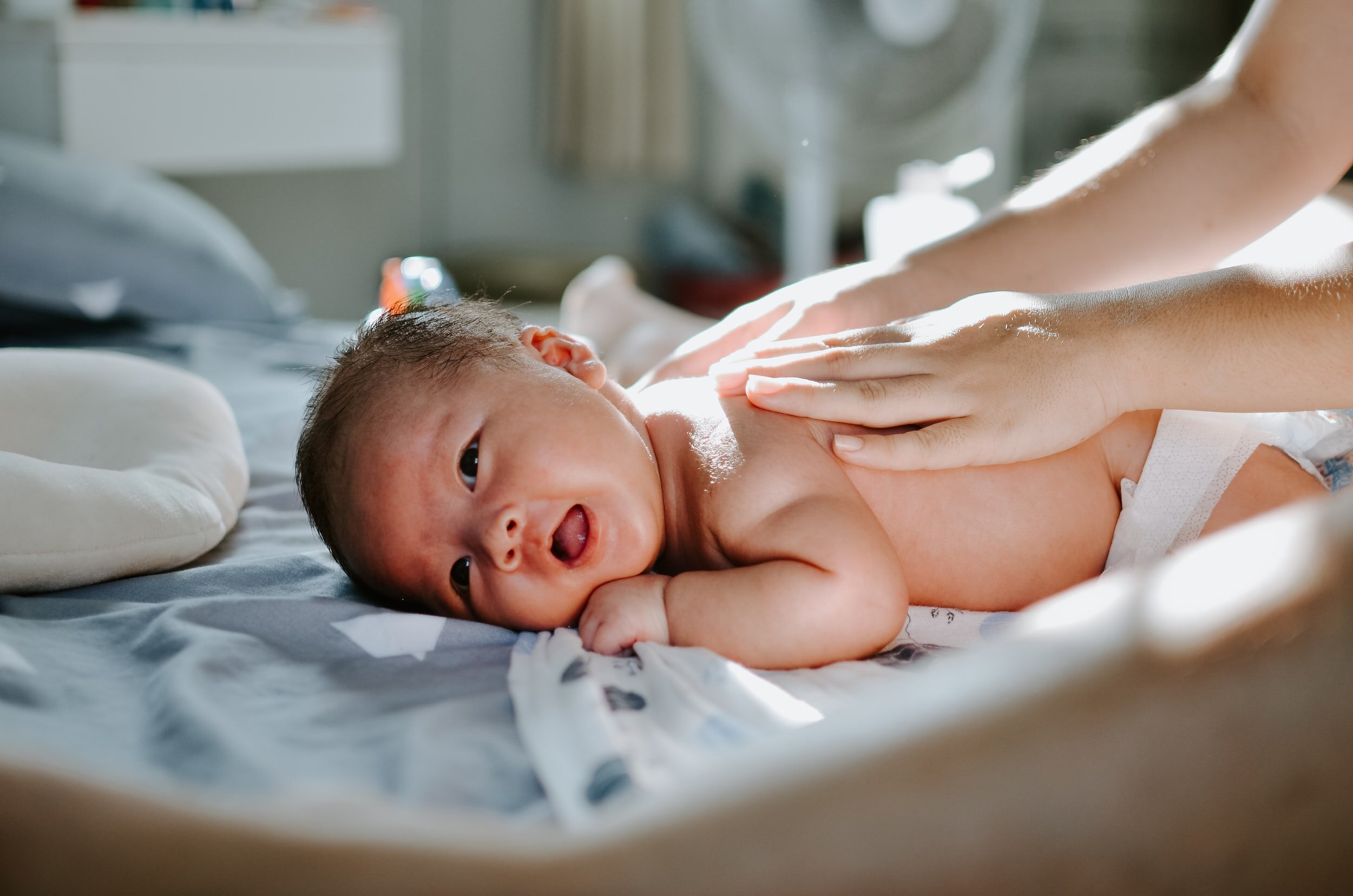 A baby lying on a bed, being gently massaged by someone's hands.