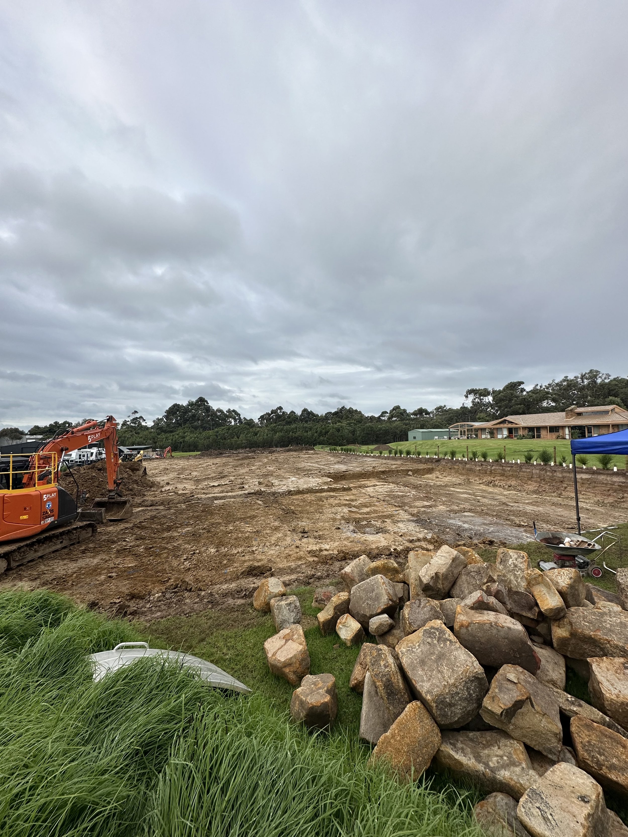 Construction site with excavator and rocks, overcast sky at Cowes