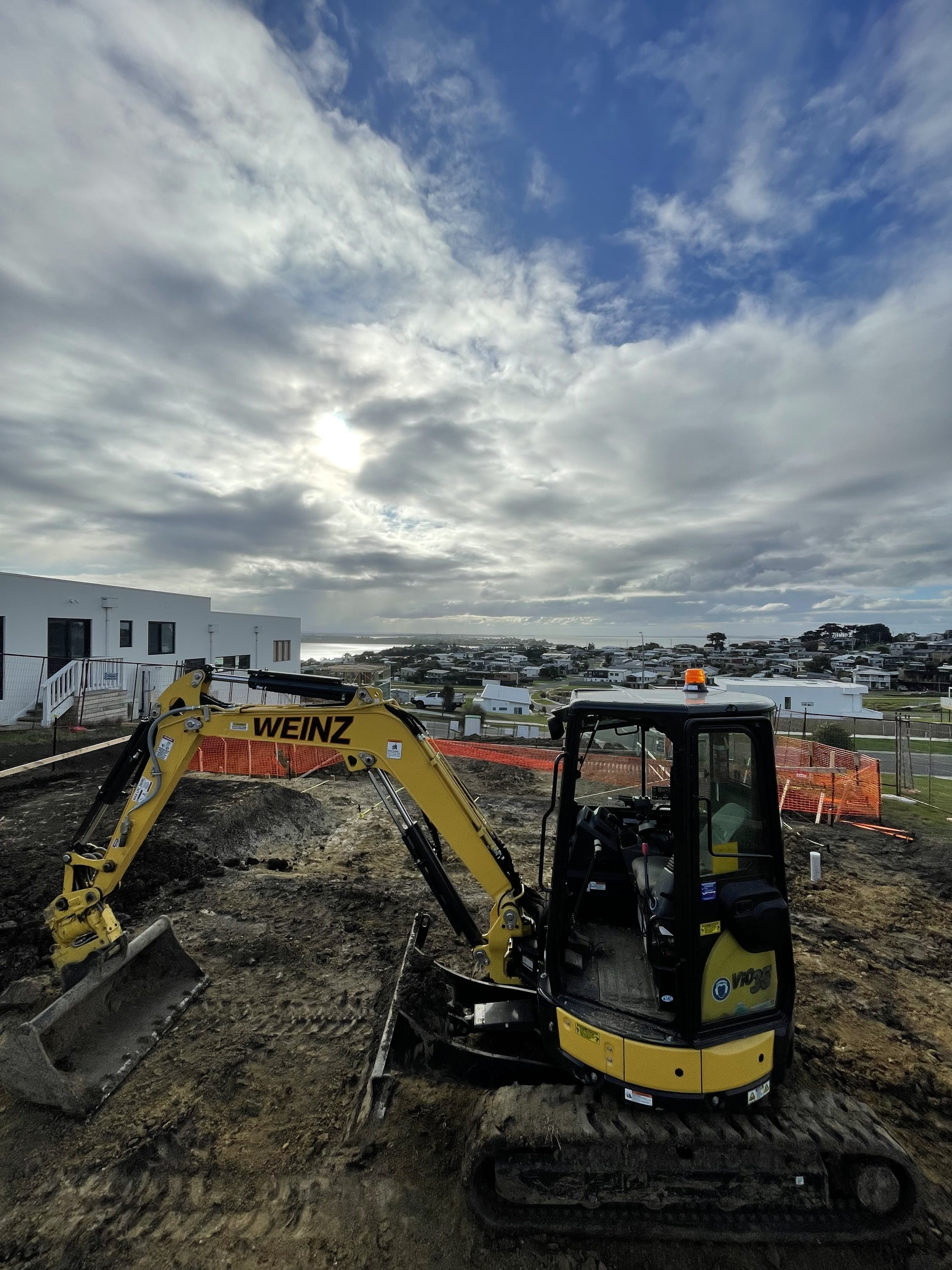 Yellow excavator at a construction site with cloudy sky and buildings in the background at San Remo