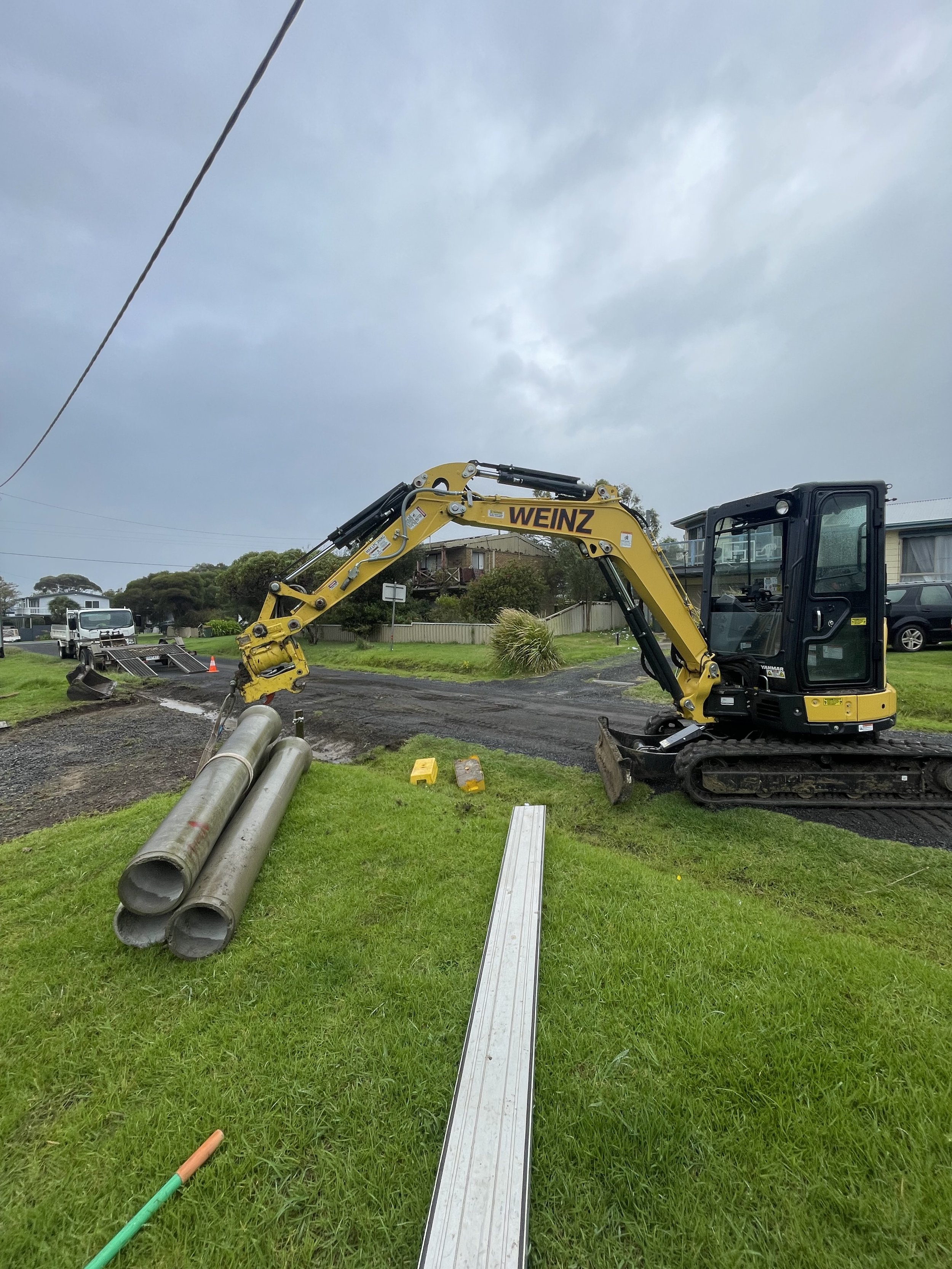 Construction site with an excavator and steel pipes on grass at Cowes