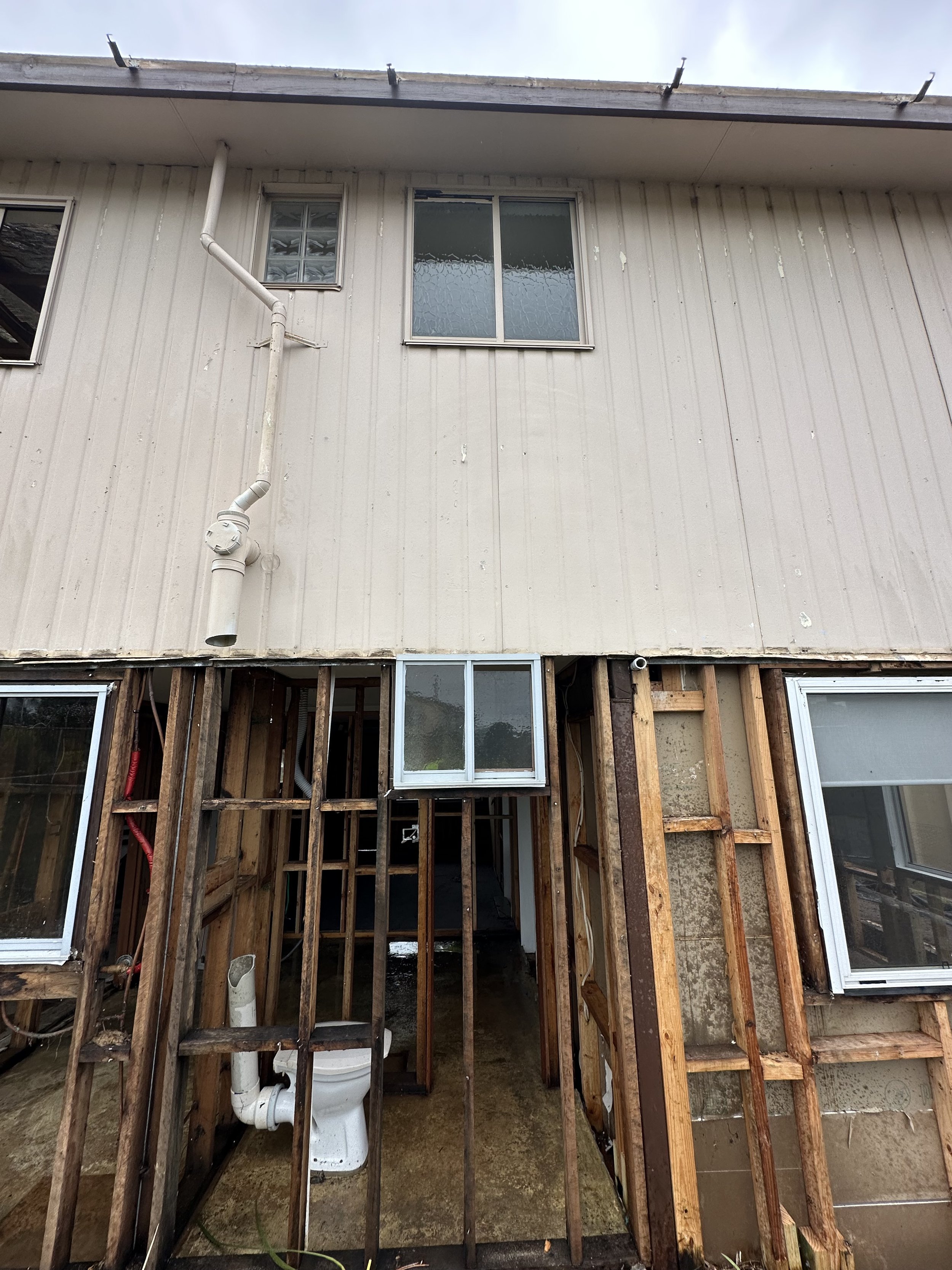 Partially demolished structure with exposed wooden framing and a toilet visible among the beams.