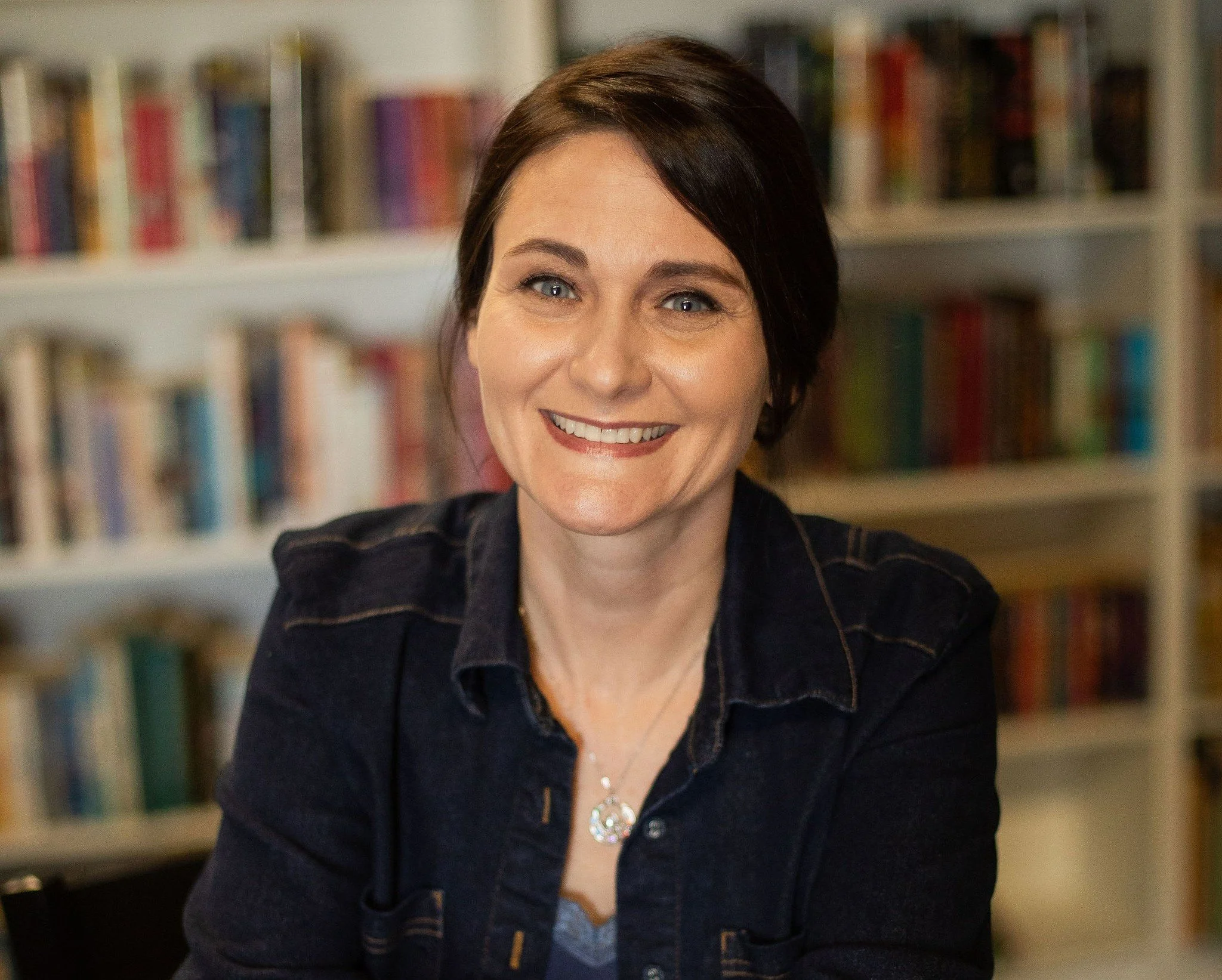 Melissa Field, wearing a dark denim jacket and sitting in front of a bookshelf.