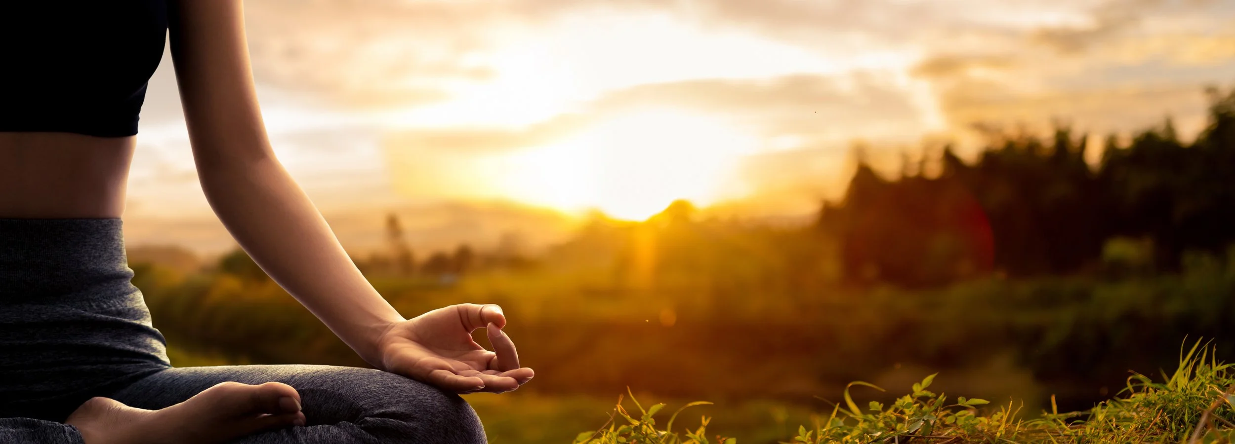 Person practicing yoga outdoors at sunset, sitting cross-legged with hand in mudra position.