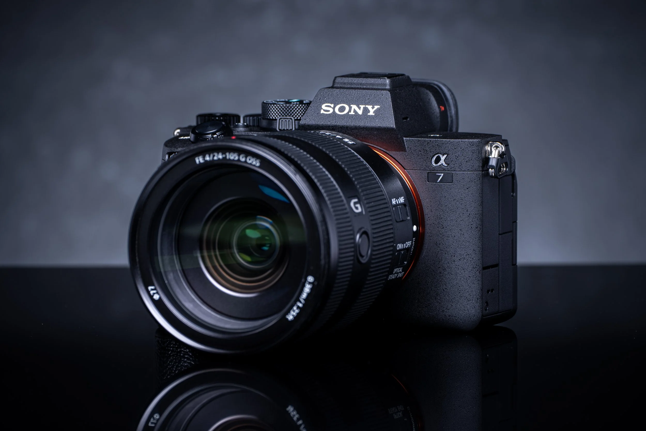 A black Sony camera with a large lens, placed on a reflective surface against a dark background.