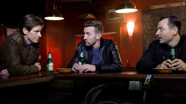 Patrick Murney portraying a character during a bar scene with fellow actors.