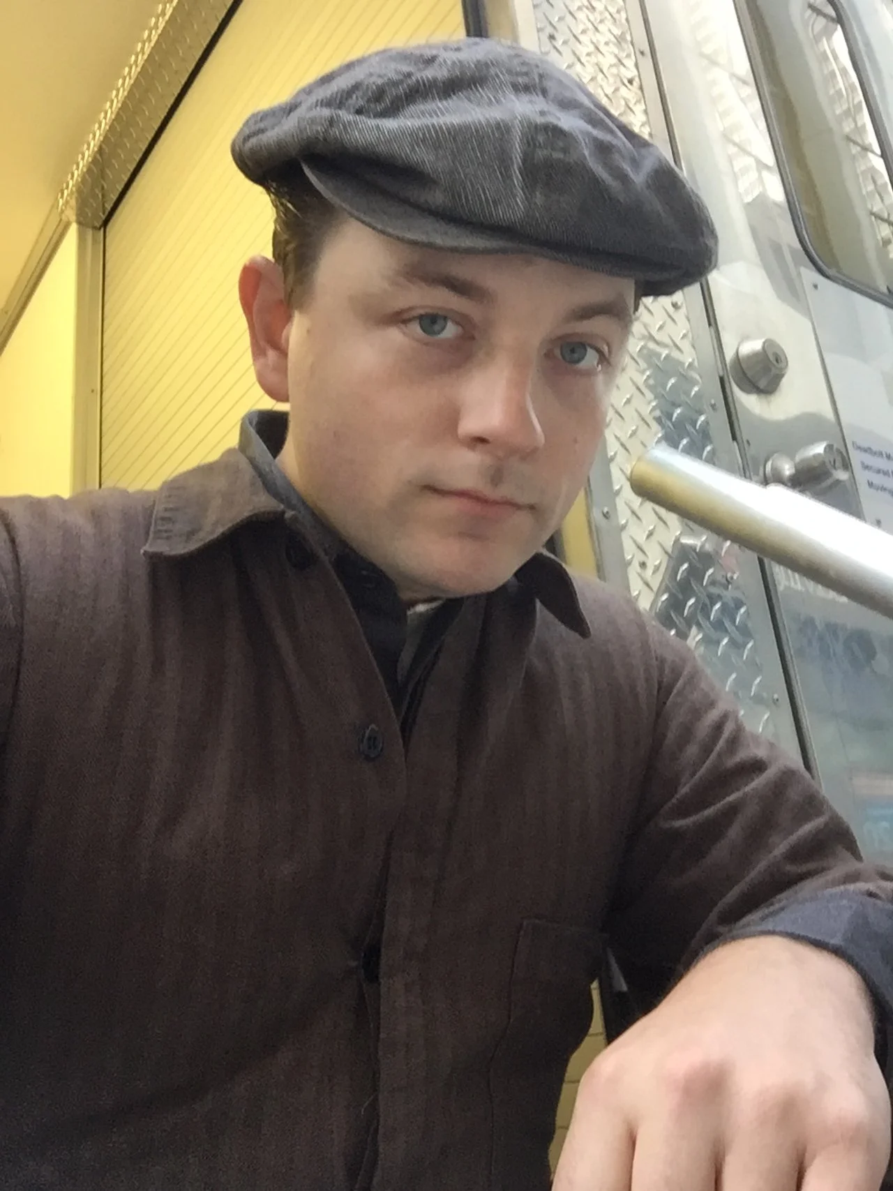 Patrick Murney wearing a flat cap in a candid behind-the-scenes portrait.