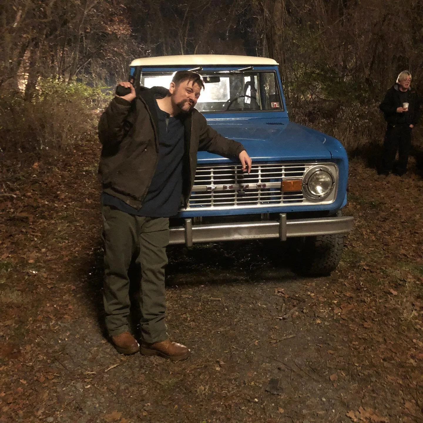 Behind-the-scenes photo of Patrick Murney on set beside a vintage blue truck.
