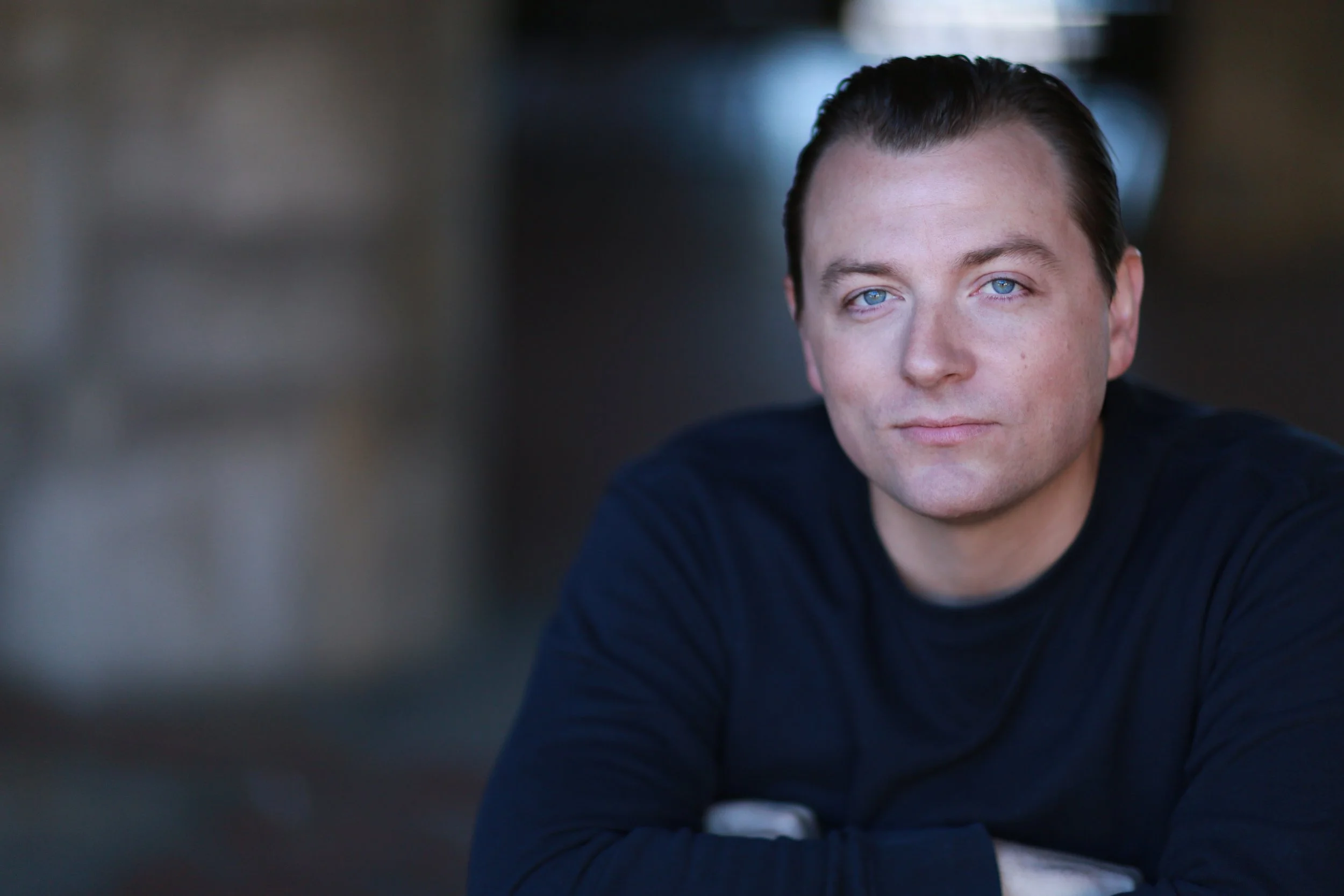 Patrick Murney portrait in a navy sweater with arms folded.