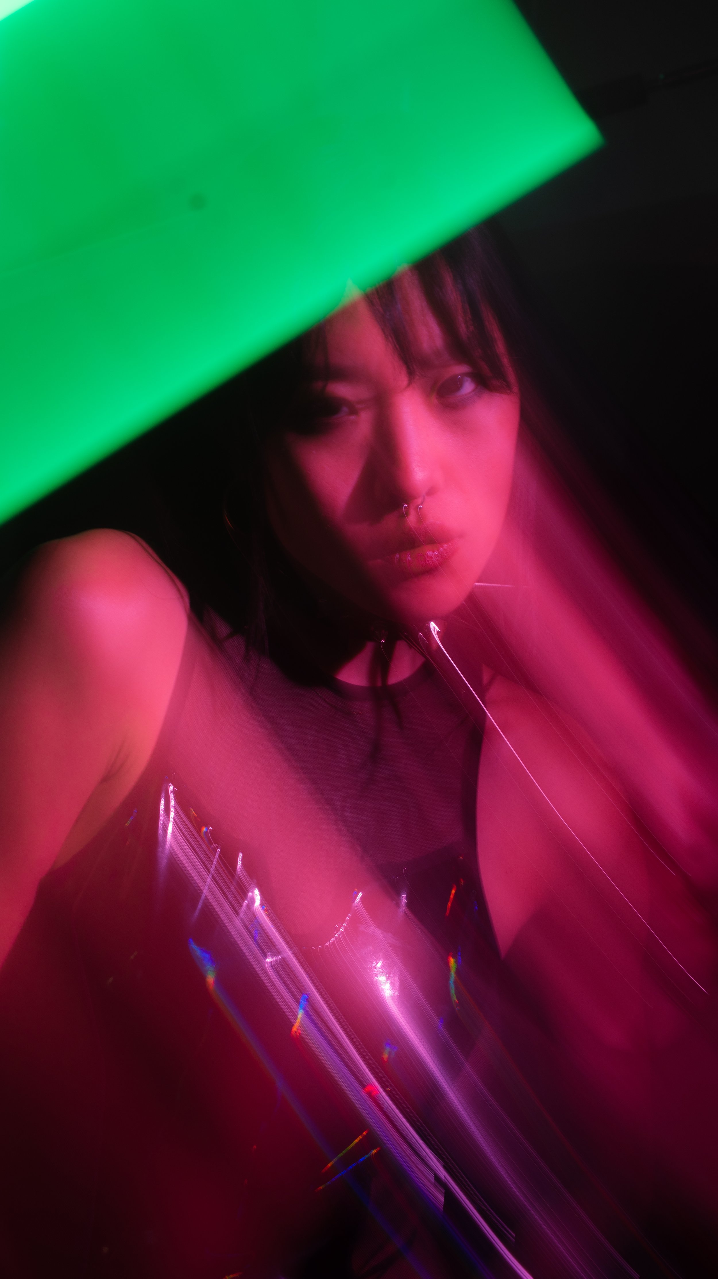Artistic portrait of a person with a green neon light and pink motion blur effect.