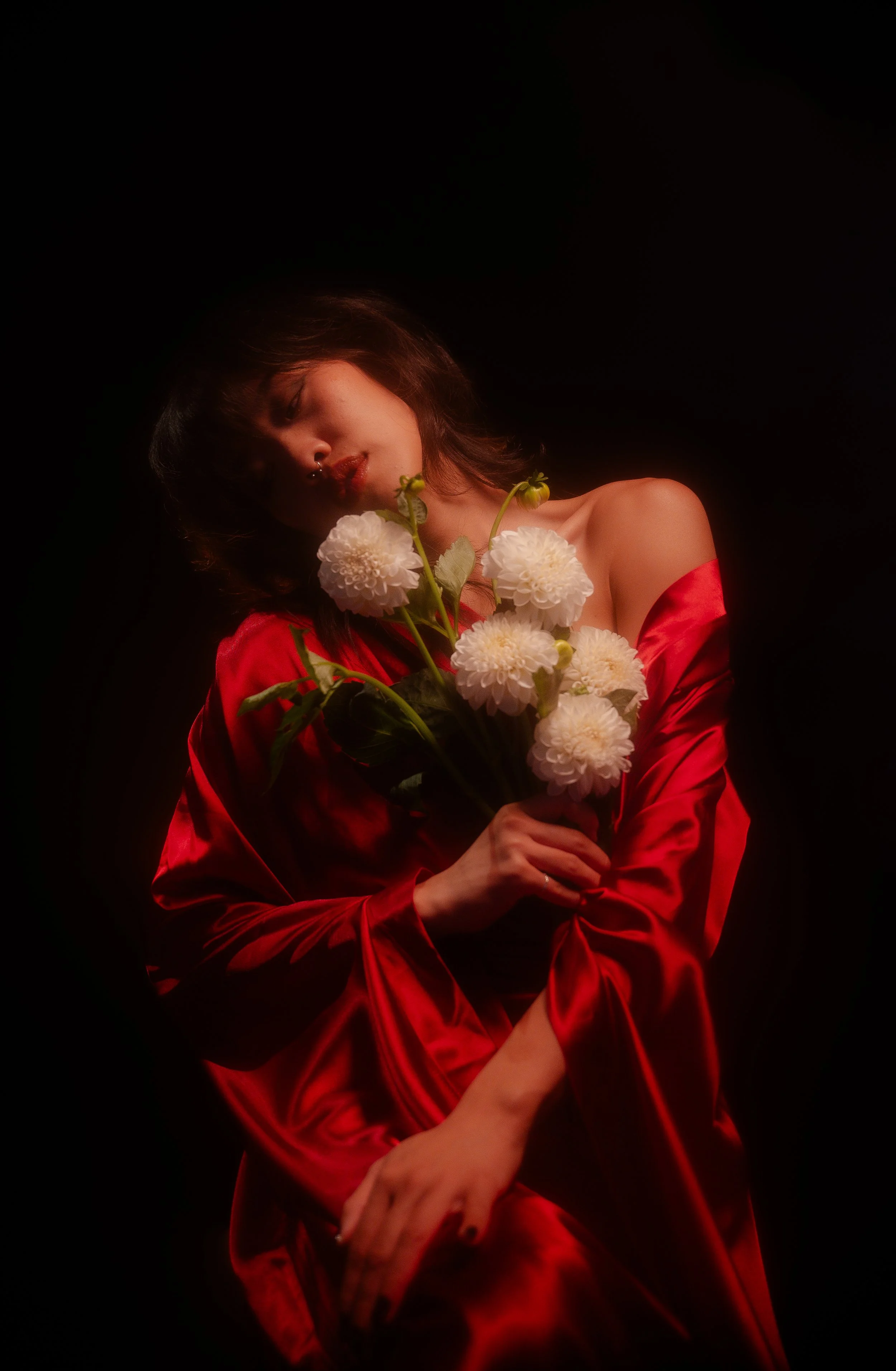 Woman in red dress holding white flowers against dark background.