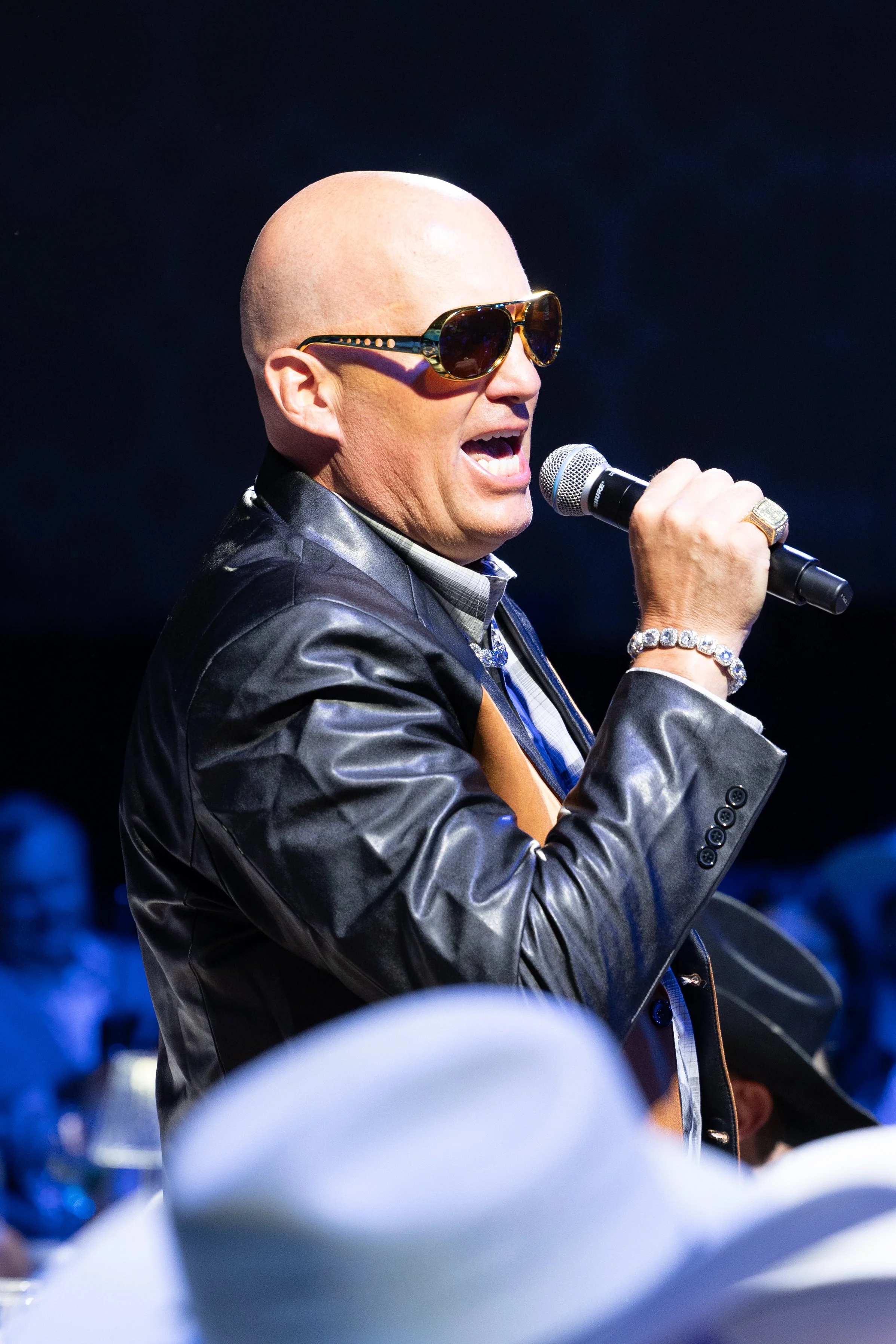 A high-energy live entertainer and MC performing with a microphone on stage during a corporate gala event dinner in the Dallas-Fort Worth area.