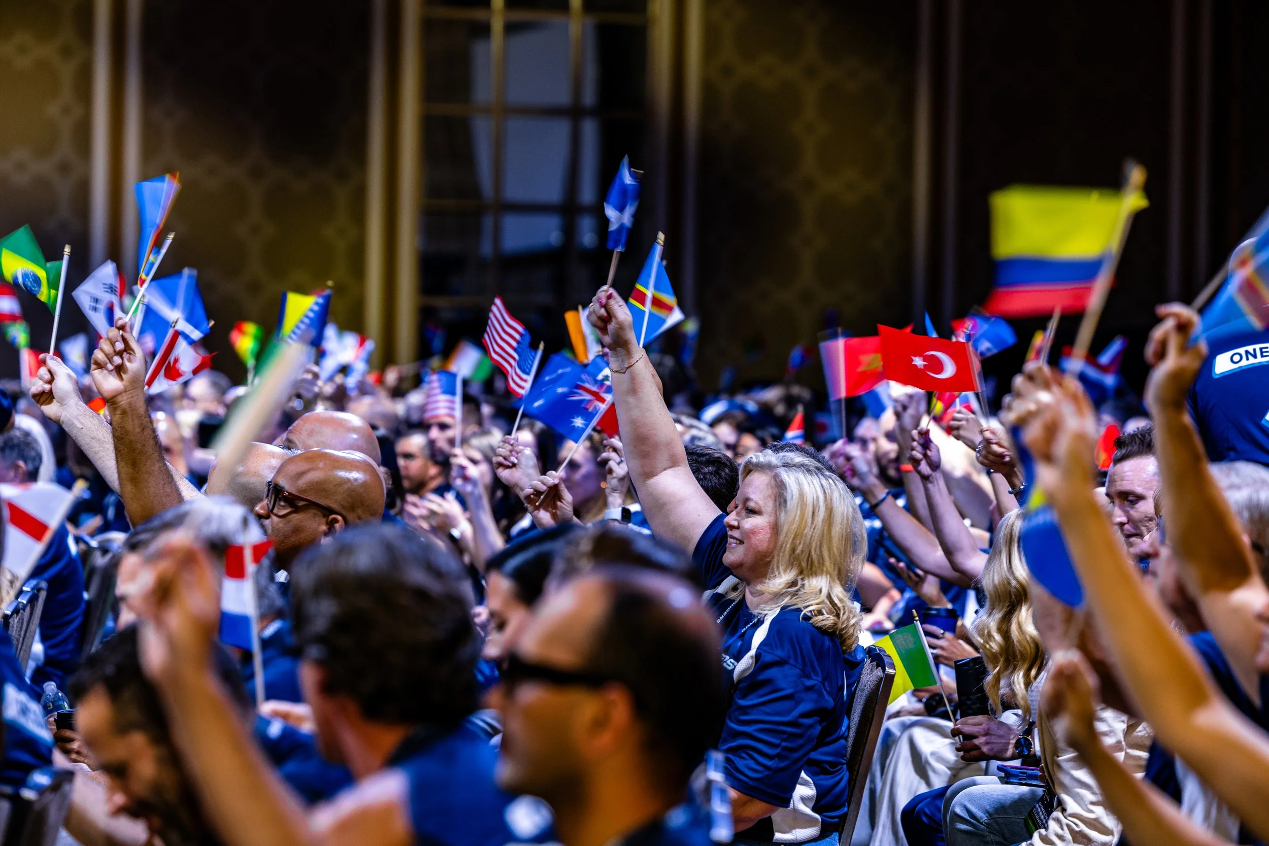 An enthusiastic audience waving international flags during a global business summit and corporate conference session in the Dallas-Fort Worth area.