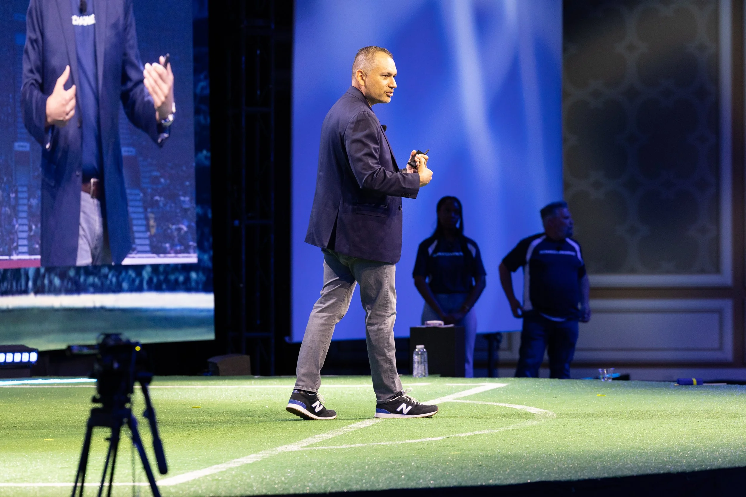 An executive keynote speaker delivering a presentation on an active main stage with large projection screens during a corporate seminar in the Dallas-Fort Worth region.