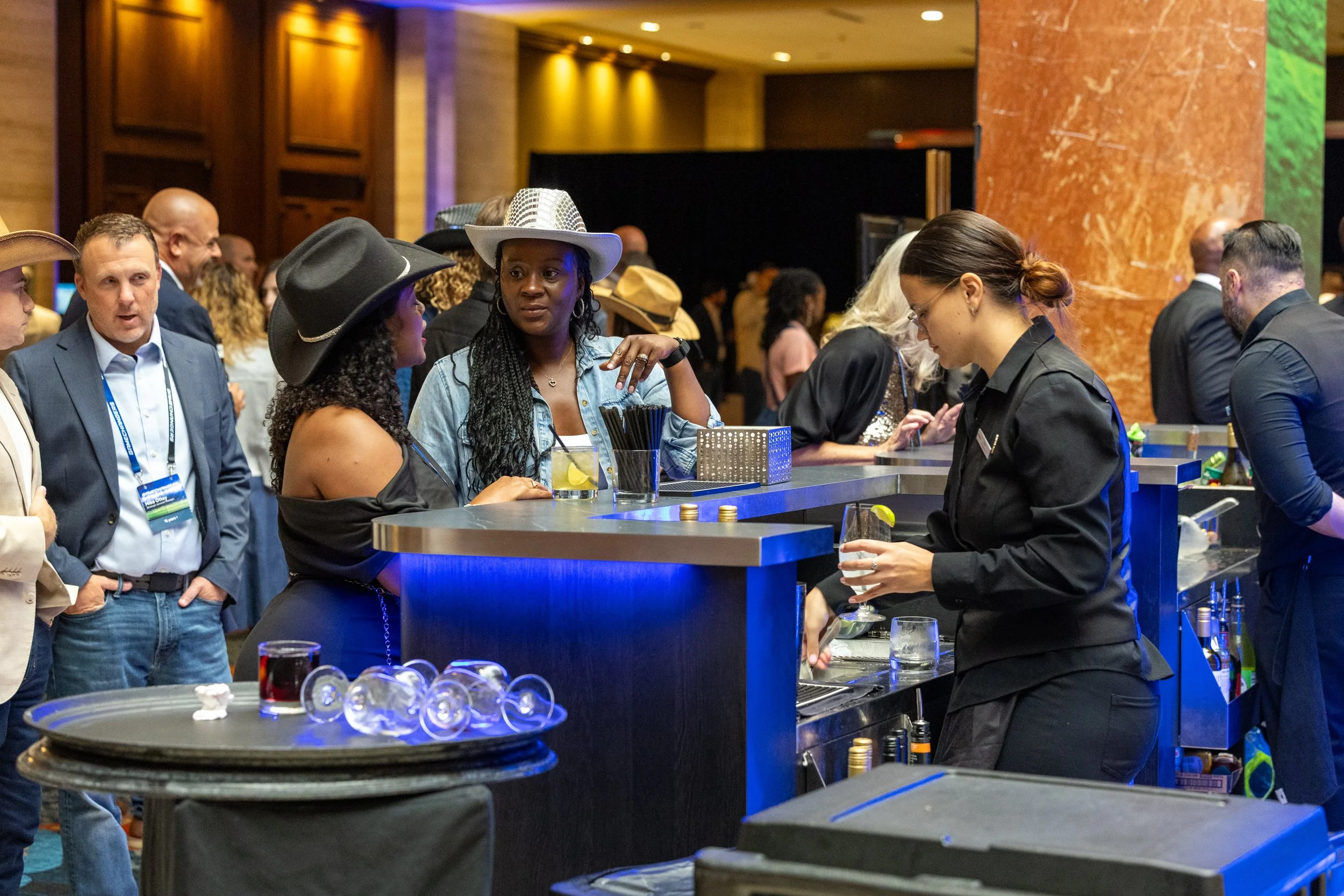 Attendees in cowboy hats ordering drinks at a modern bar with blue LED lighting during a corporate networking reception in Dallas-Fort Worth.