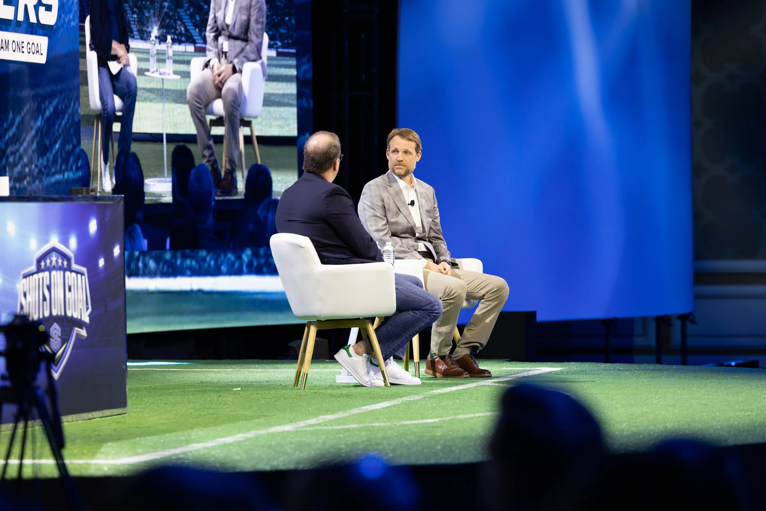 Two corporate executives conducting a fireside chat on a main stage panel during a business convention in Dallas-Fort Worth, showcasing professional event production and stage lighting.
