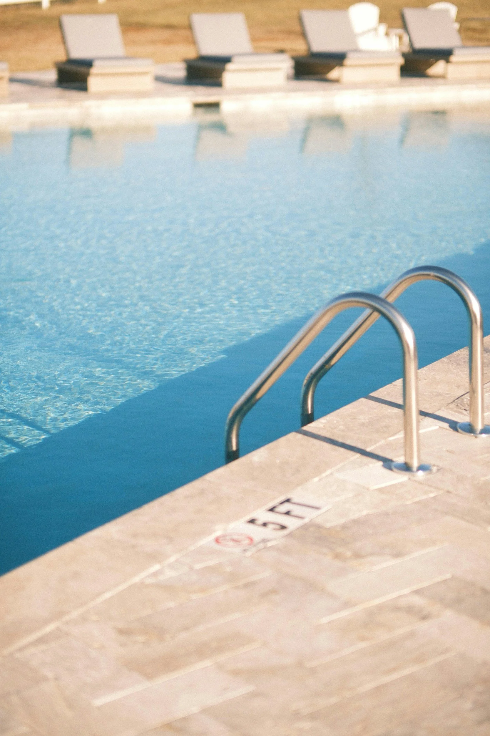 A swimming pool with a metal handrail and a depth marker indicating 5 feet, surrounded by a concrete deck.