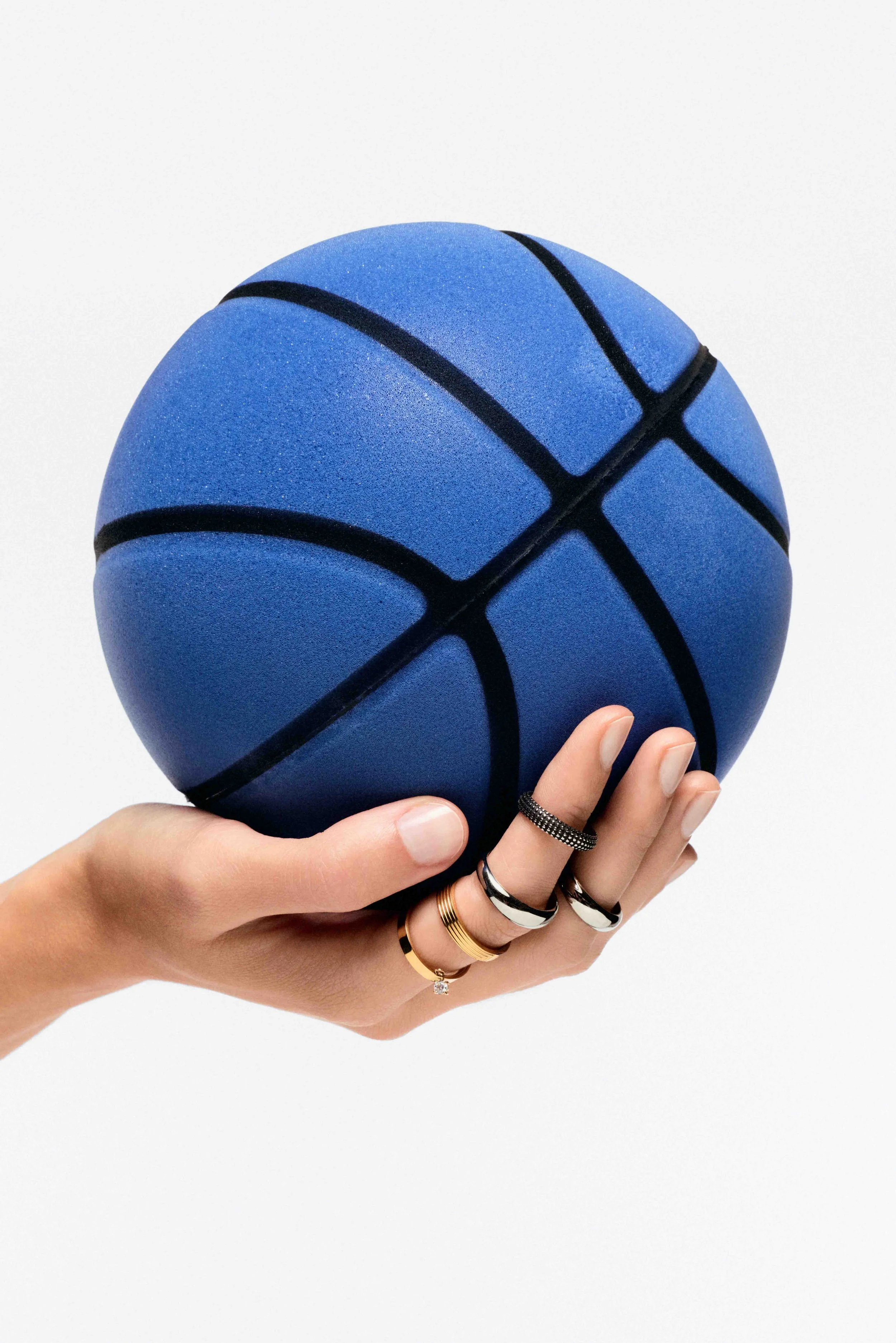 A hand holding a blue foam basketball with black lines, against a plain white background.