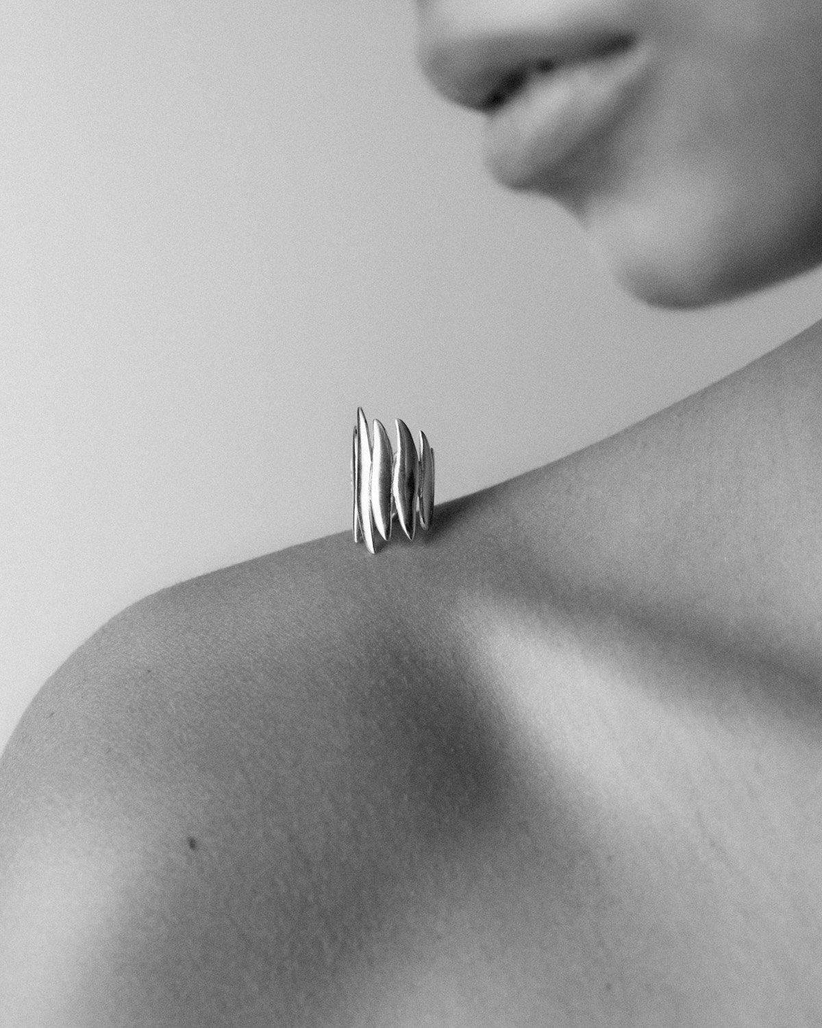 Close-up black and white photo of lips and a shoulder with a stack of rings resting on the shoulder.