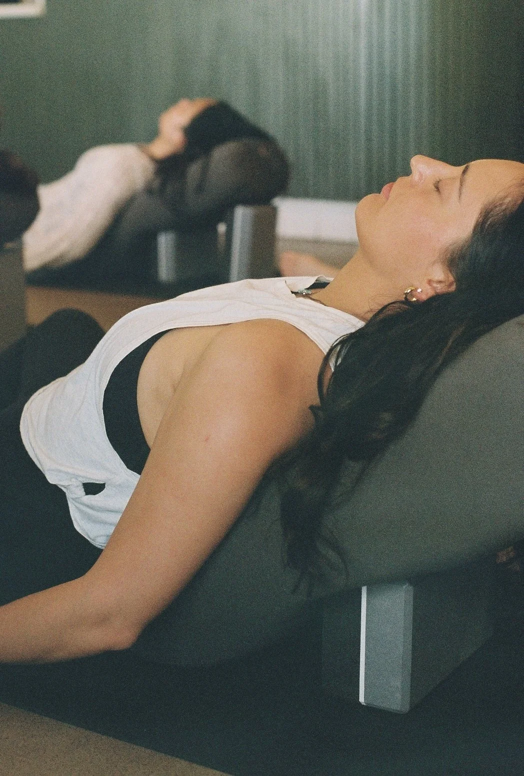 Close up of yoga students laying face-up on bolsters with blocks underneath for Salamba Supta Baddha Konasana
