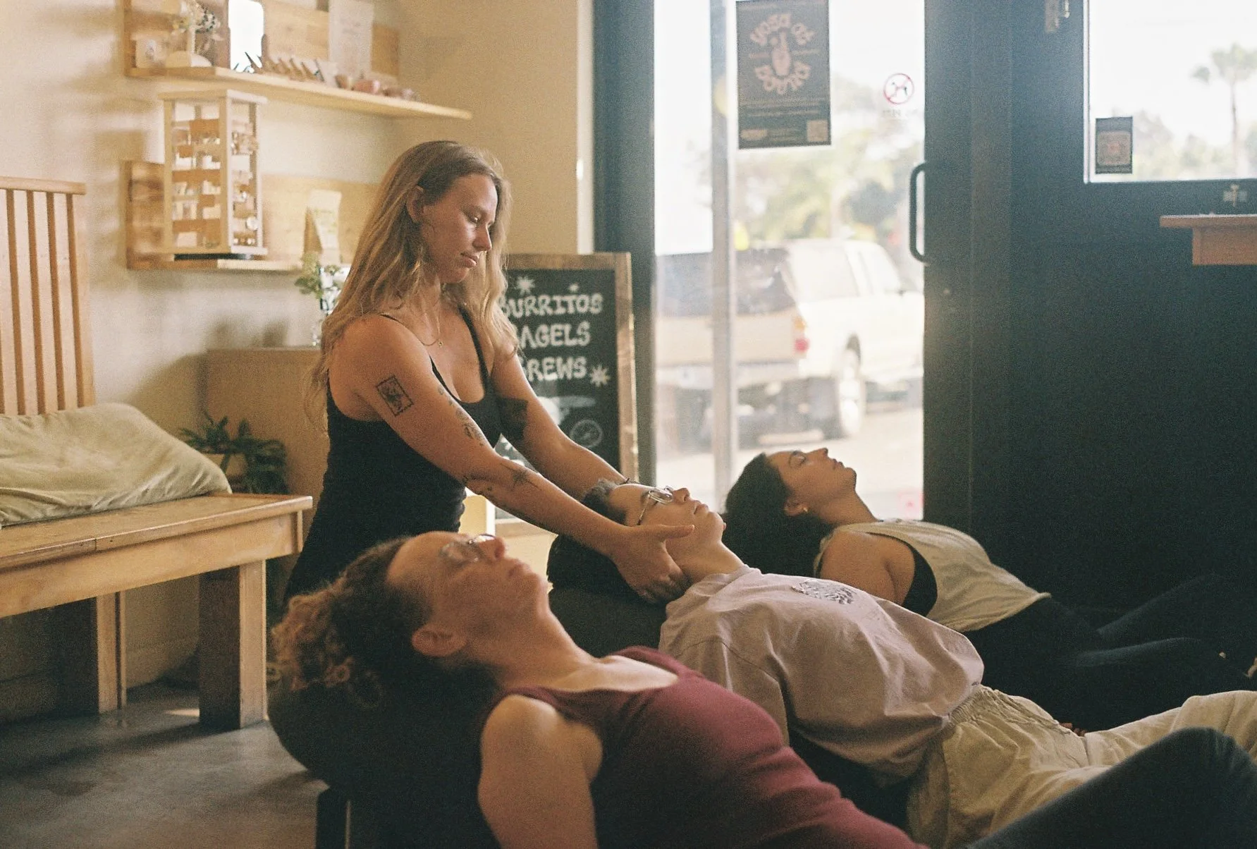 Yoga students laying face-up on bolsters while yoga teacher provides hands-on adjustments