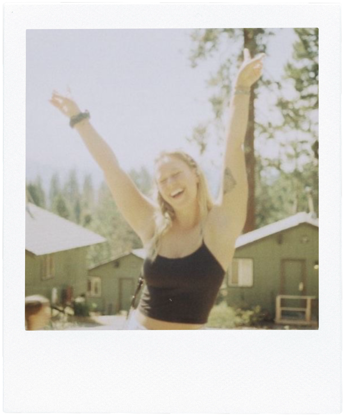 35mm film photo of Sarah Madore with arms raised overhead in a joyful manner. Framed with a white border that resembles an instant film photo. Link to "About Me" webpage