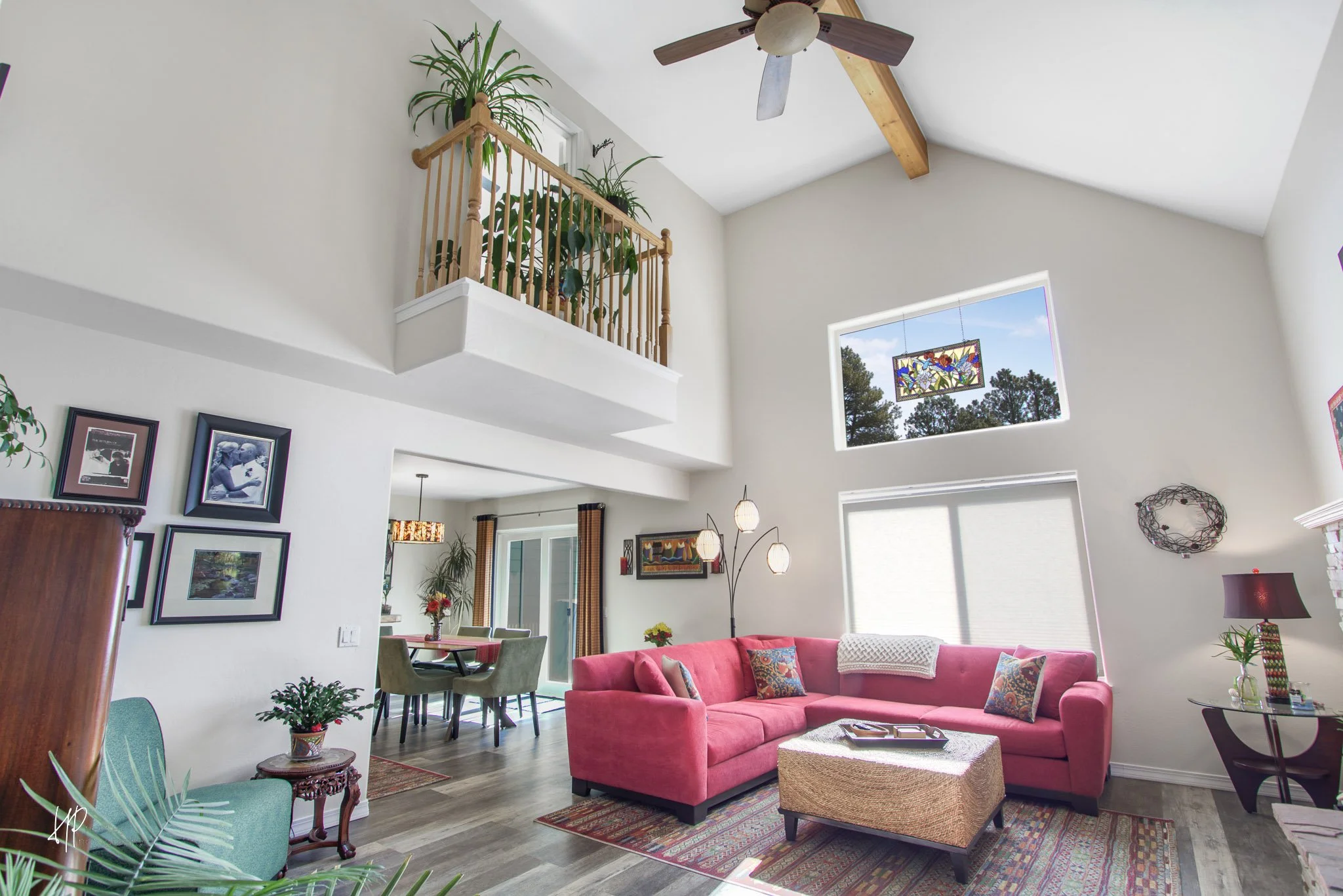 Living room with high ceiling, pink sectional sofa, large windows, and ceiling fan.