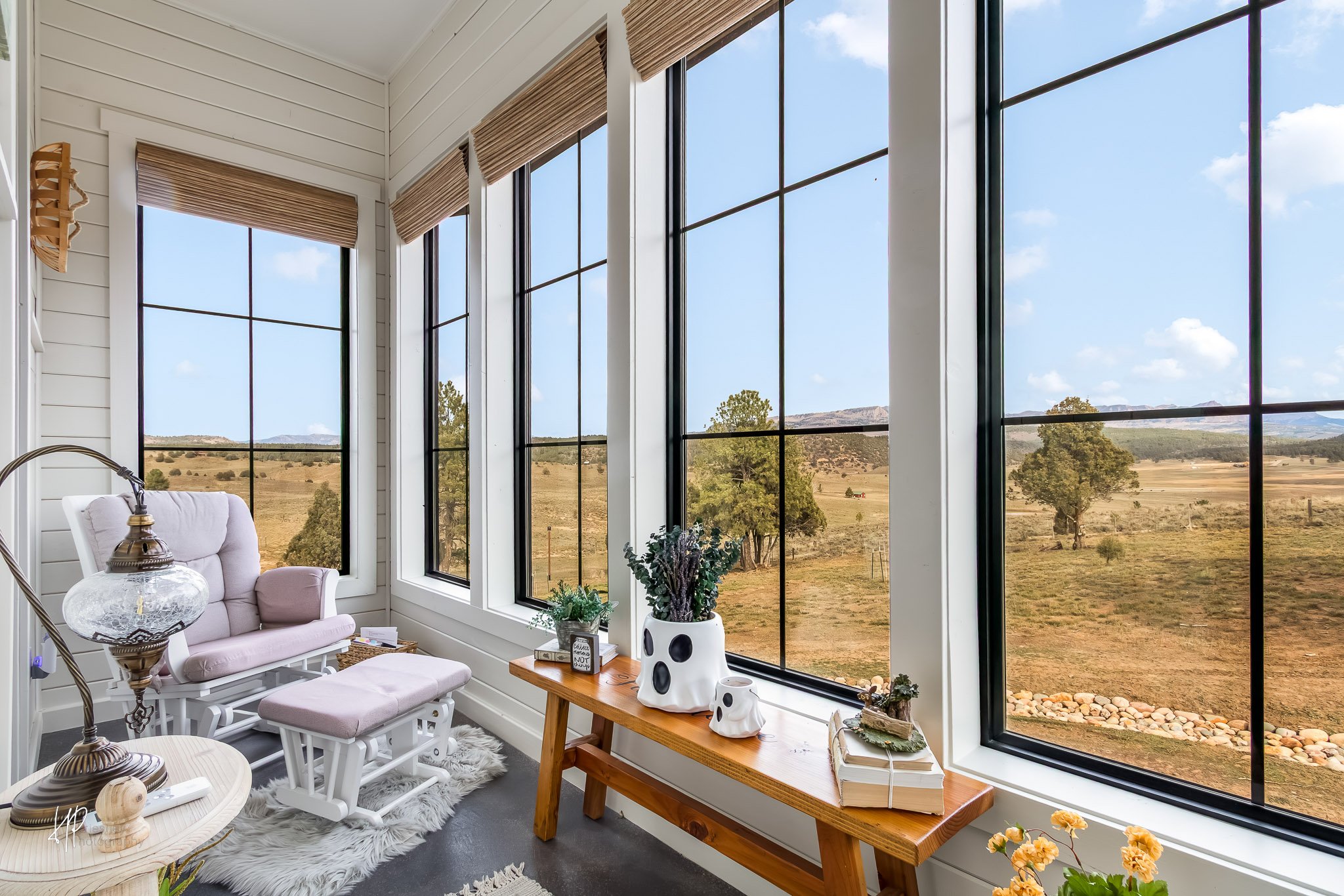 Sunroom with large windows showing a scenic rural landscape with trees, hills, and a blue sky.