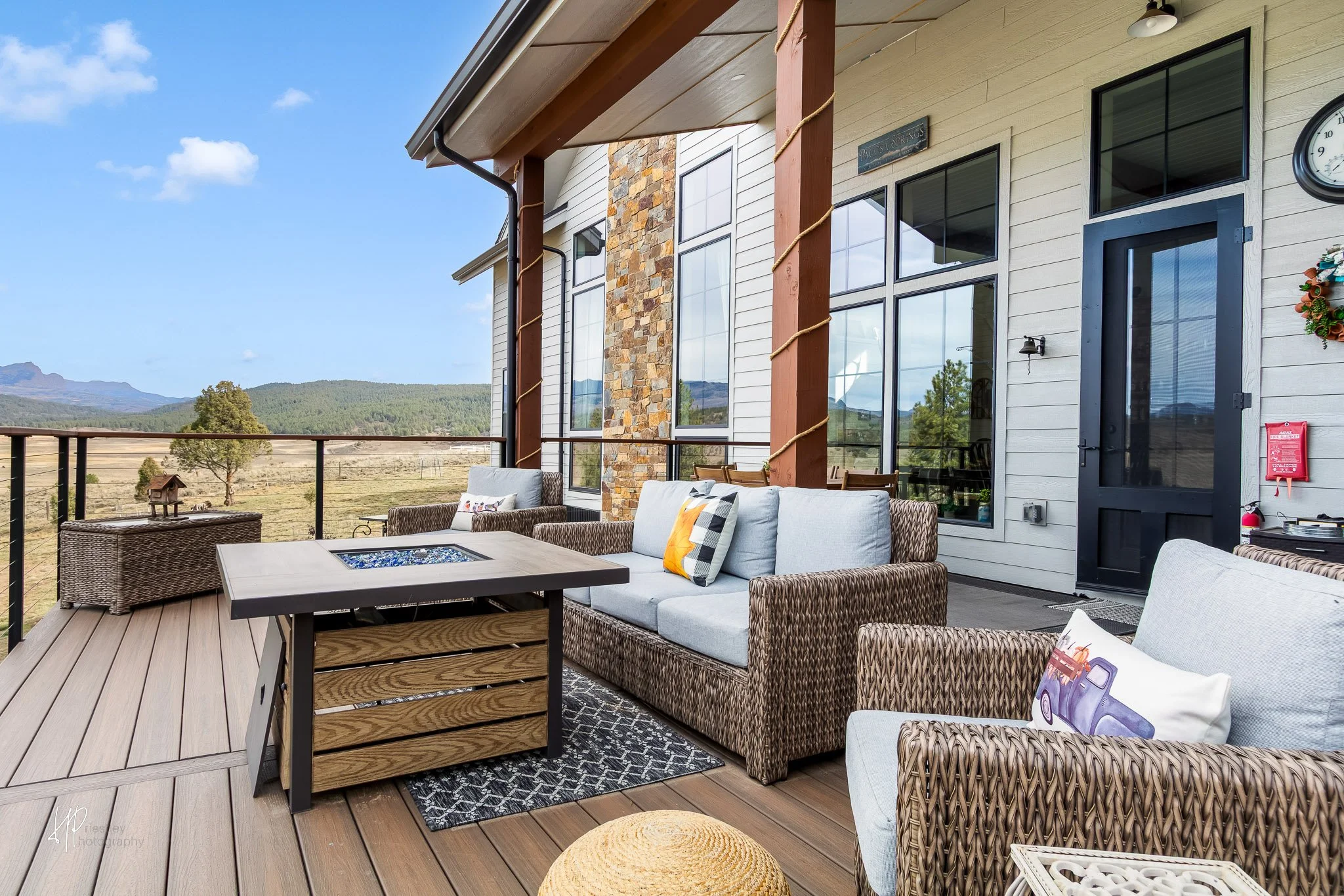 Outdoor patio with wicker and fabric seating, a fire pit table, and scenic mountains in the background.