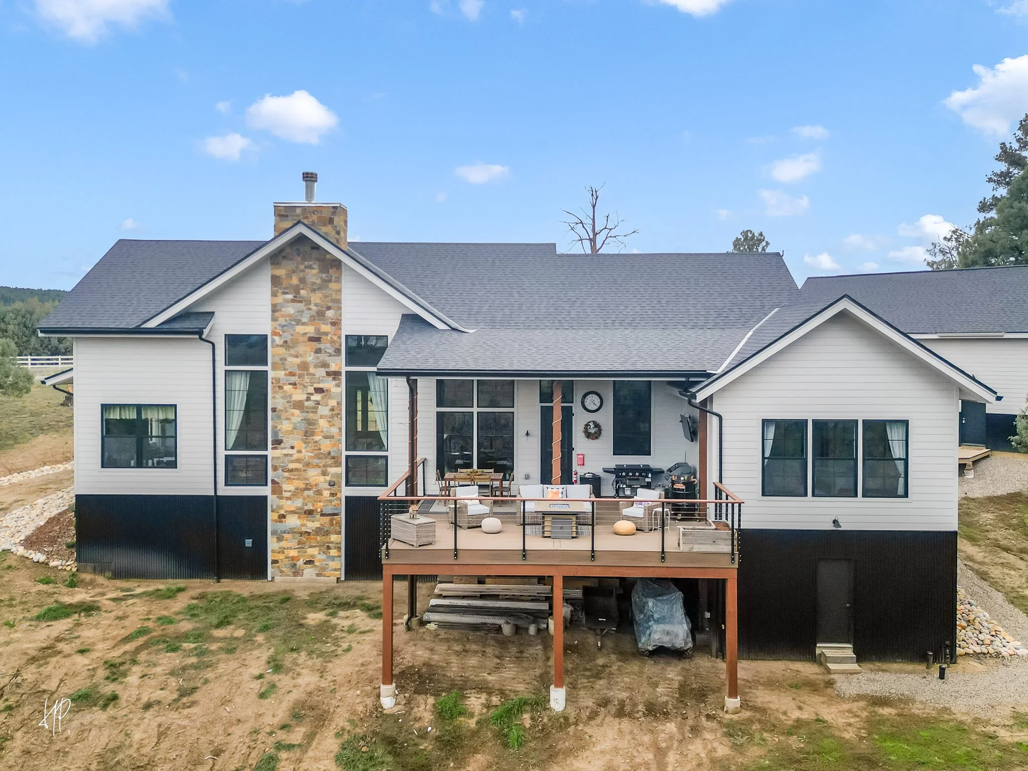 Newly constructed house with a large deck, outdoor furniture, a grill, and a view of the backyard with trees and grass.