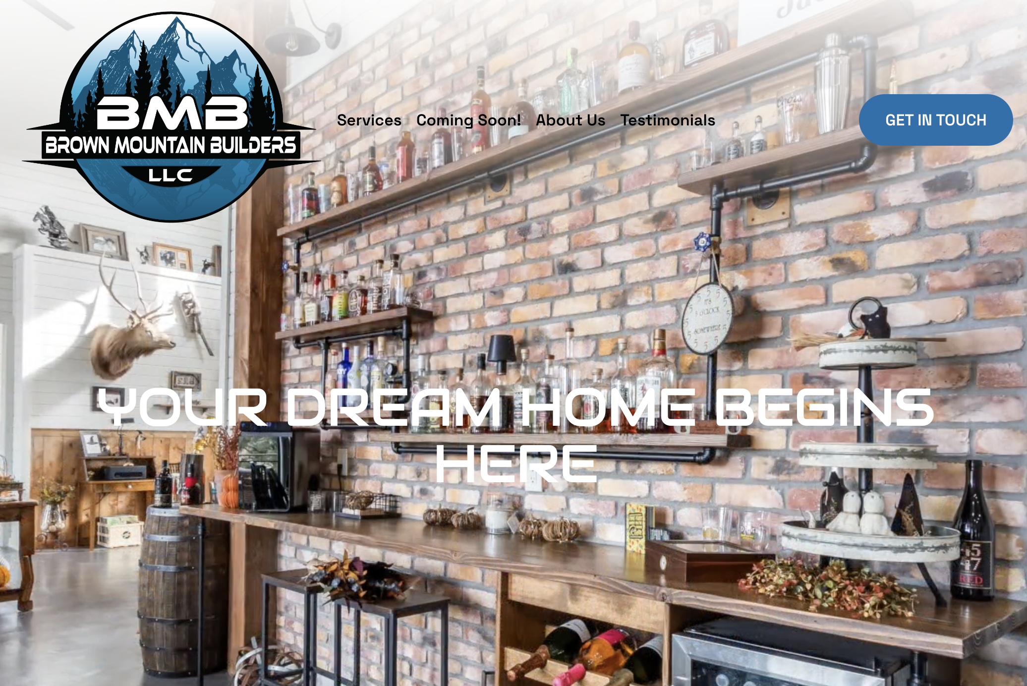 Interior of a rustic bar or restaurant with a brick wall, wooden shelves holding bottles, and a mounted deer head. Overlaid text says 'YOUR DREAM HOME BEGINS HERE', and there is a logo for Brown Mountain Builders LLC at the top left.