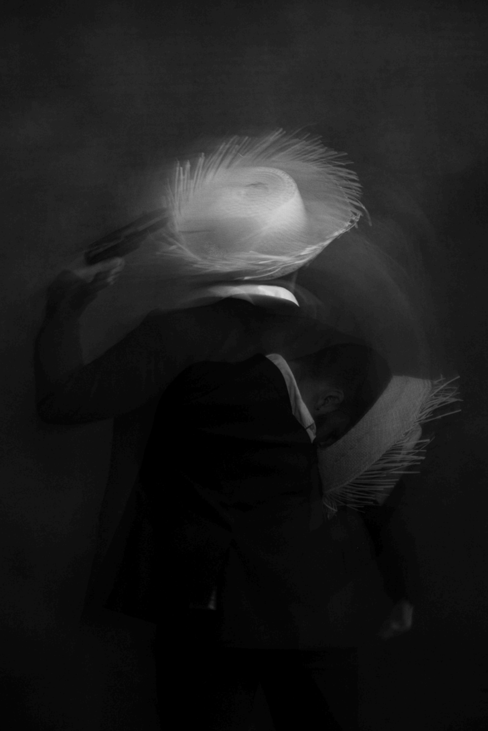 Black and White blurred image of person in straw hat holding gun to their head