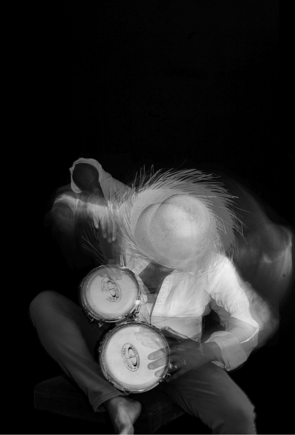Black and White blurred image of person wearing straw hat as they play bongos