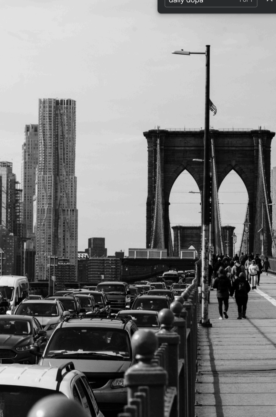 Black and White image of cars stuck in traffic on bridge as pedestrian walk on sidewalks next to it