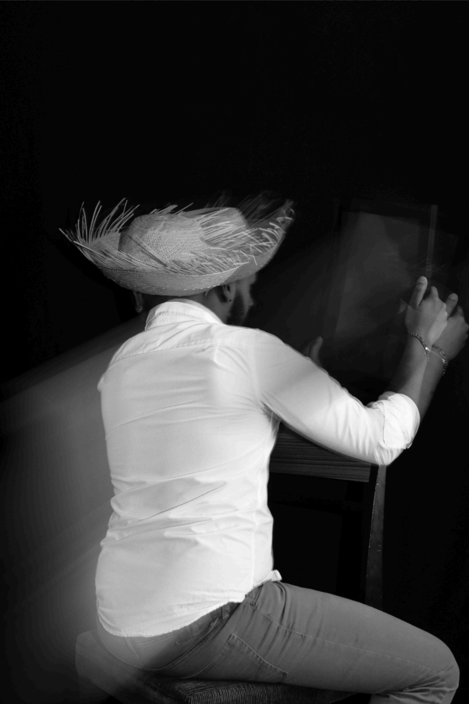 Black and White blurred image of person in straw hat holding a large wooden item