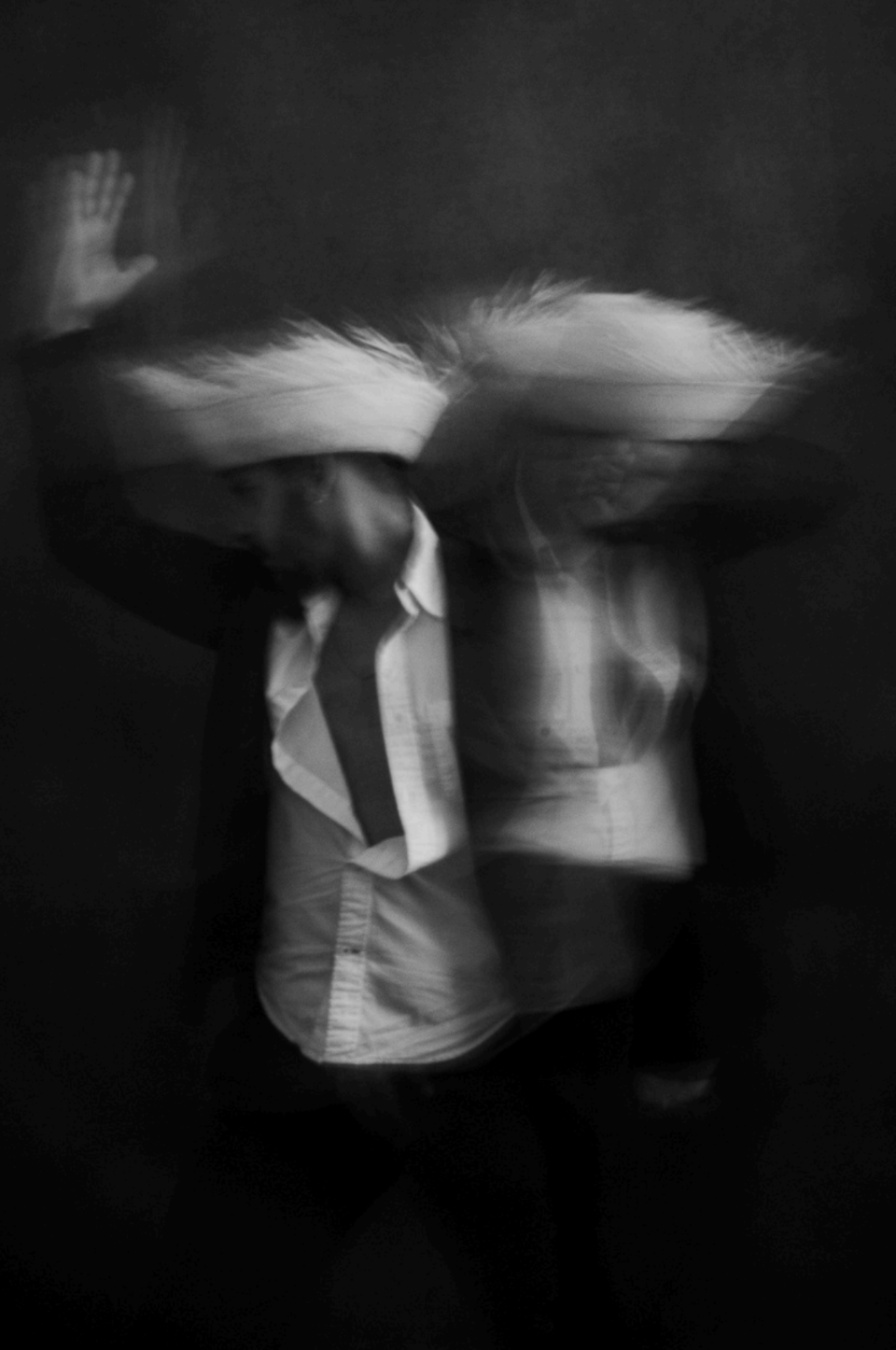 Black and White blurred image of person in straw hat with hand in air