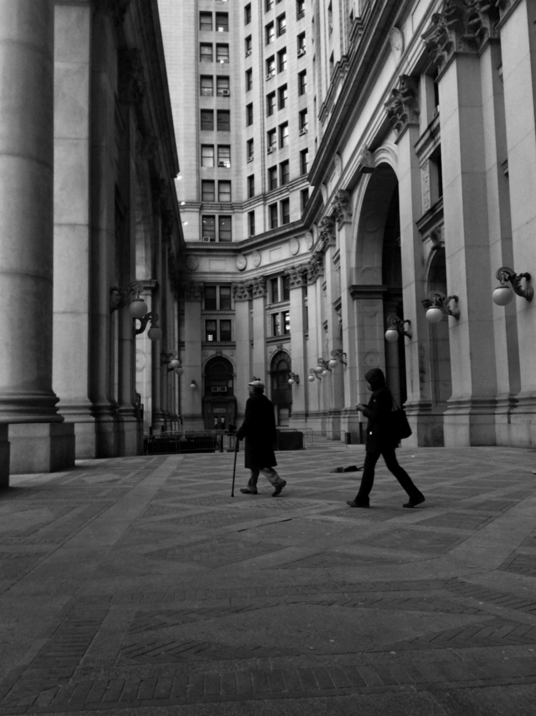Black and White image of two people walking through an open-air courtyard in the middle of a collection of stone buildings
