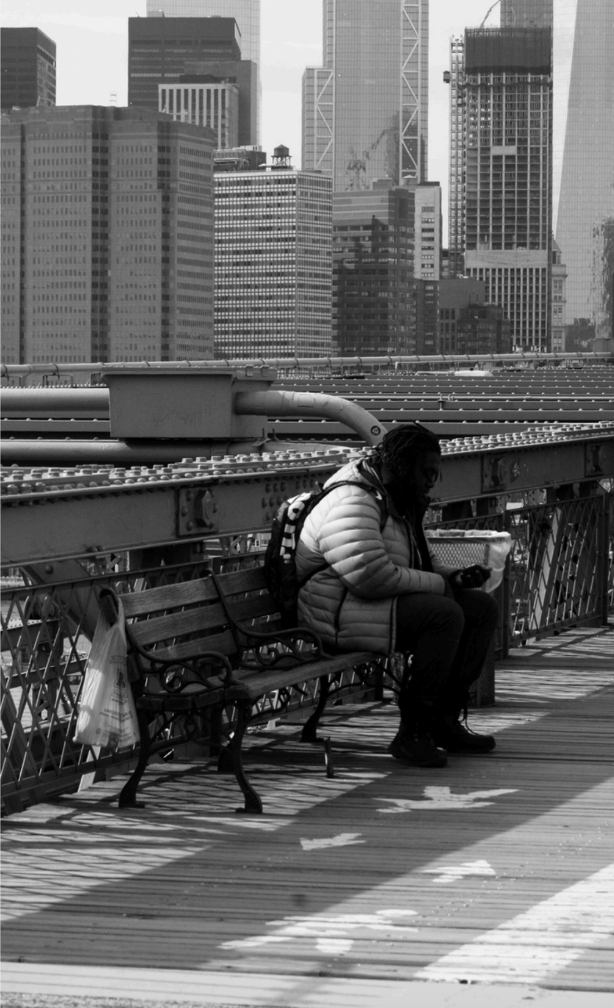 Black and White image of person sitting on bench on top of boardwalk