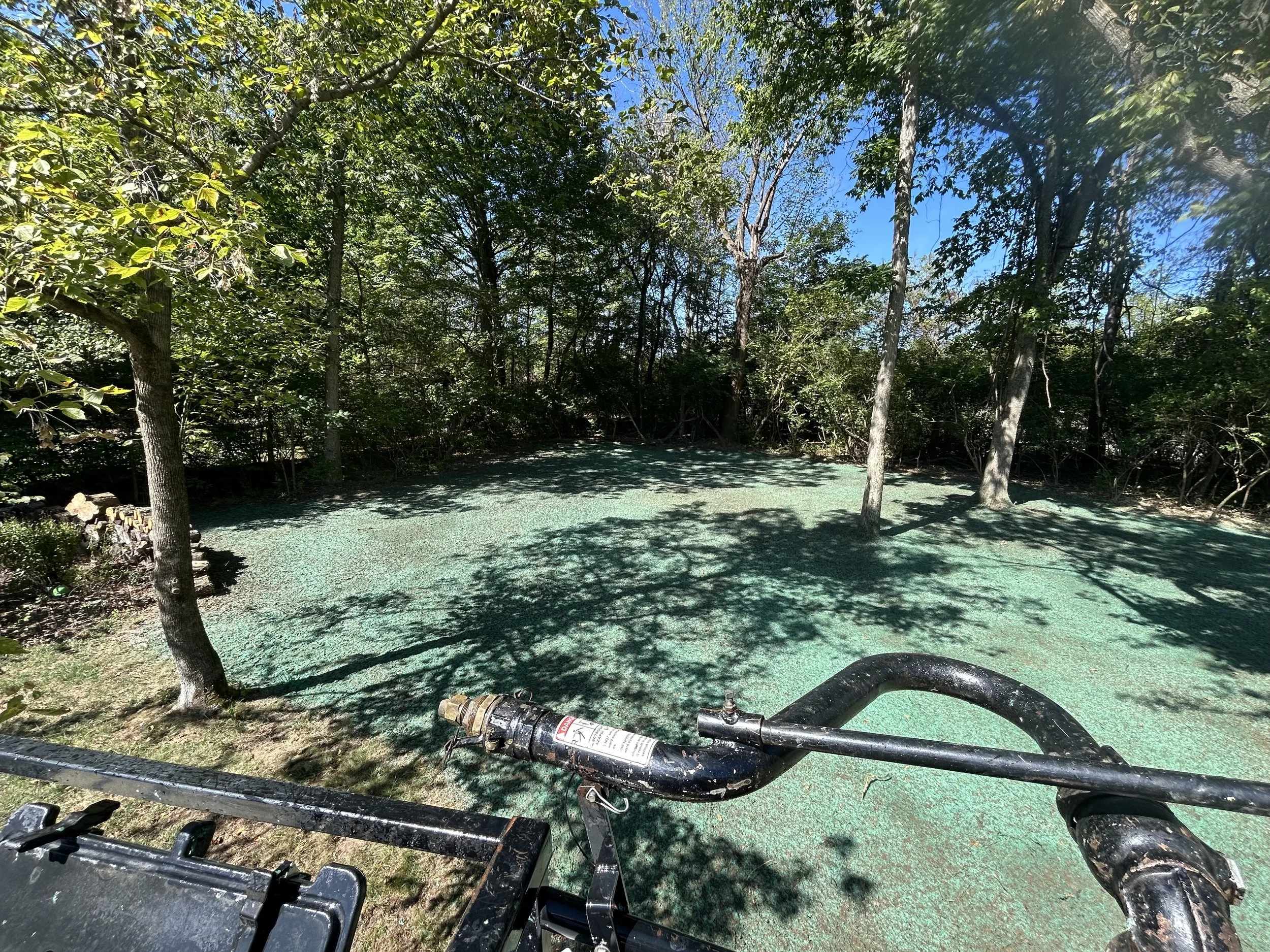 A lawn mower on a grassy area with trees and a clear blue sky in the background.