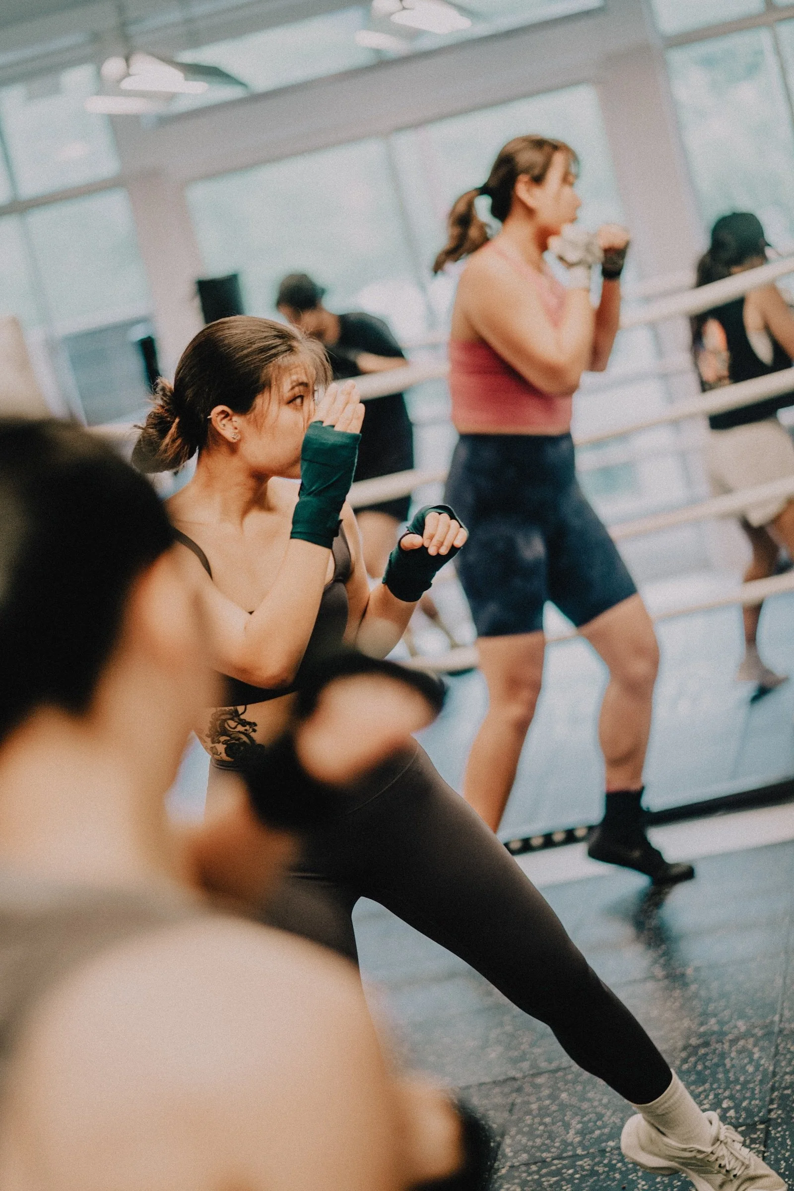Women shadowboxing in a group boxing class at Sweat Science Studio, with a boxer in green hand wraps stepping into her stance in the foreground.