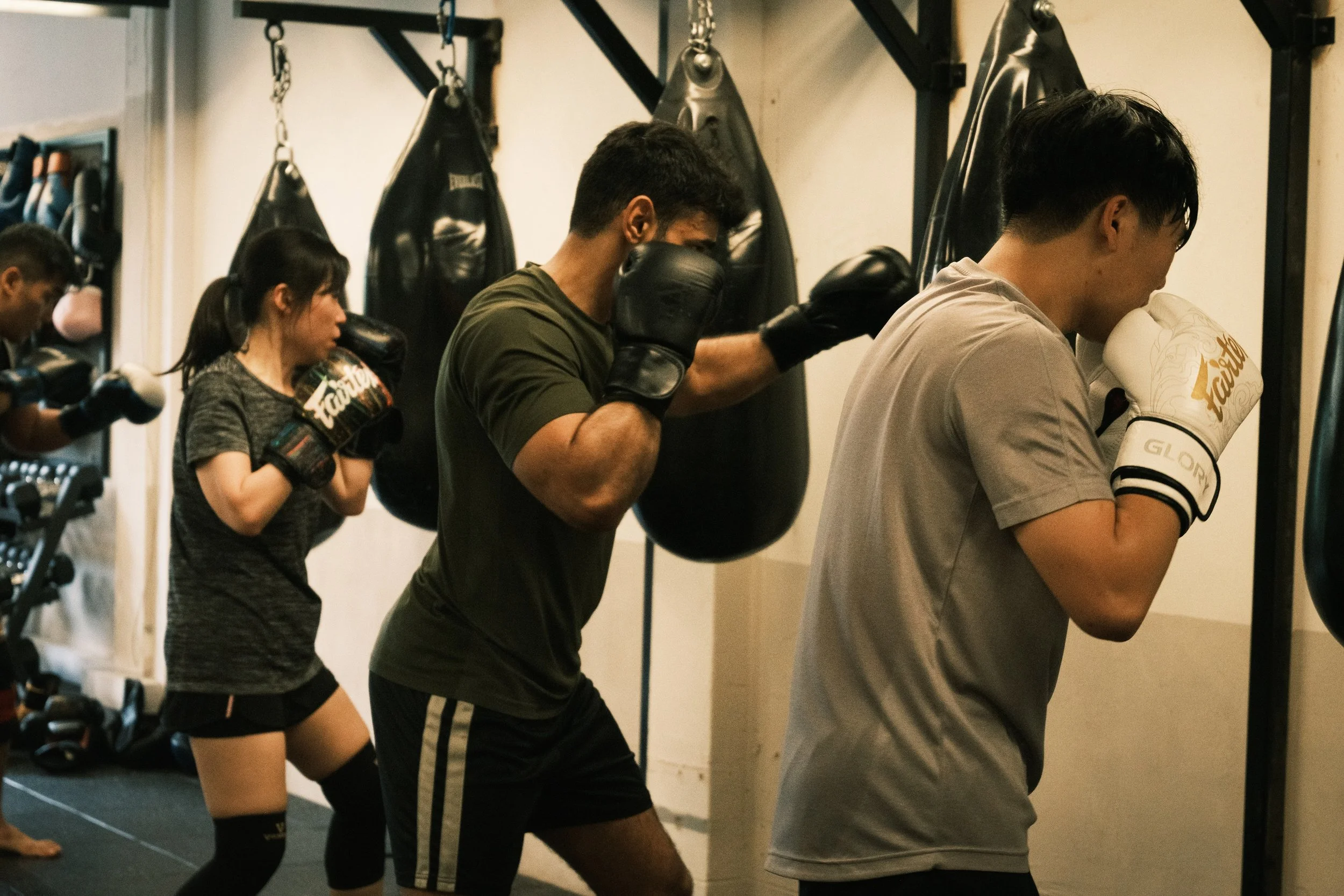 Three members throwing punches at heavy bags during a group boxing class at Sweat Science Studio, Clarke Quay, Singapore