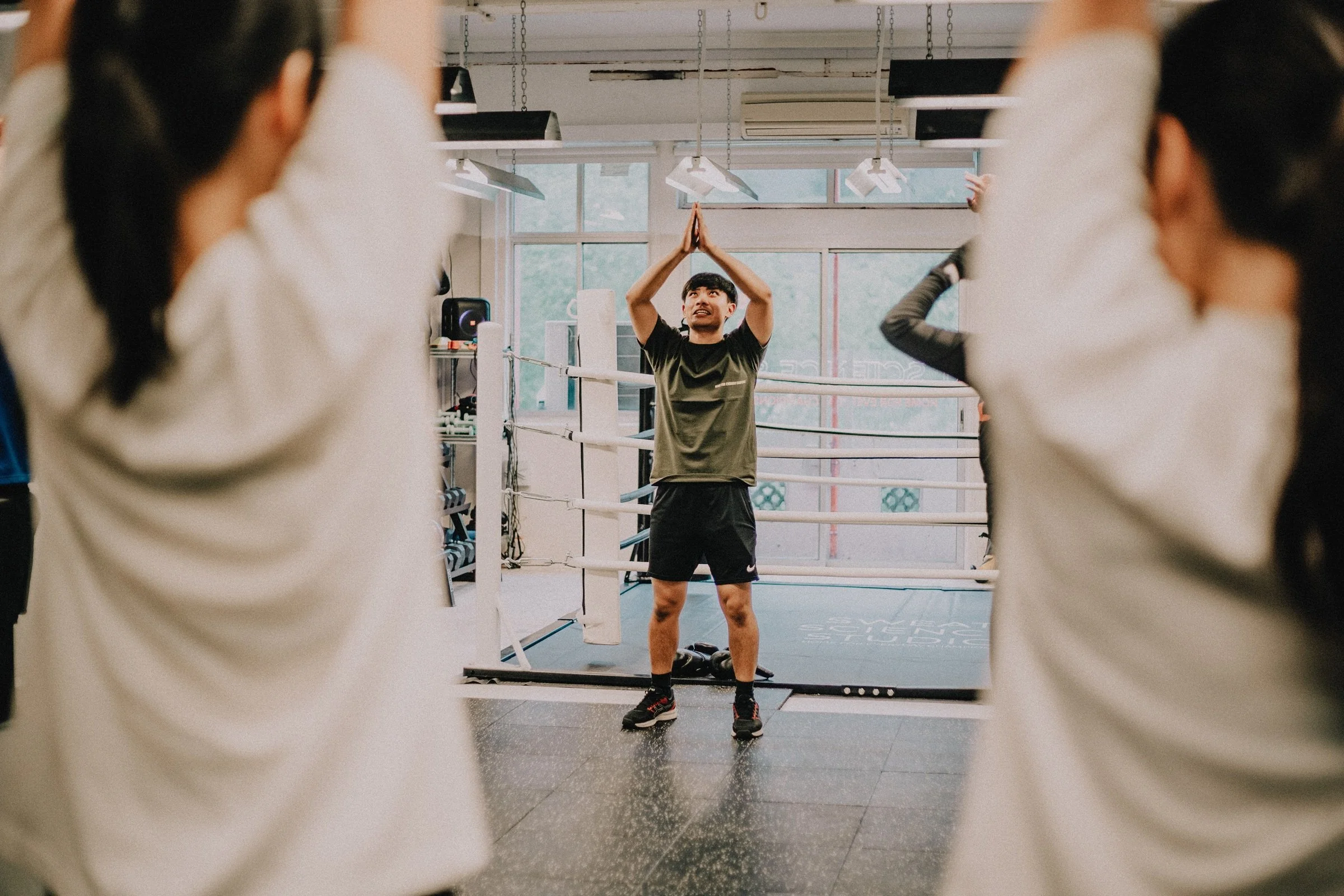 Boxing coach leading a warm-up stretch beside the ring at Sweat Science Studio, Clarke Quay Singapore