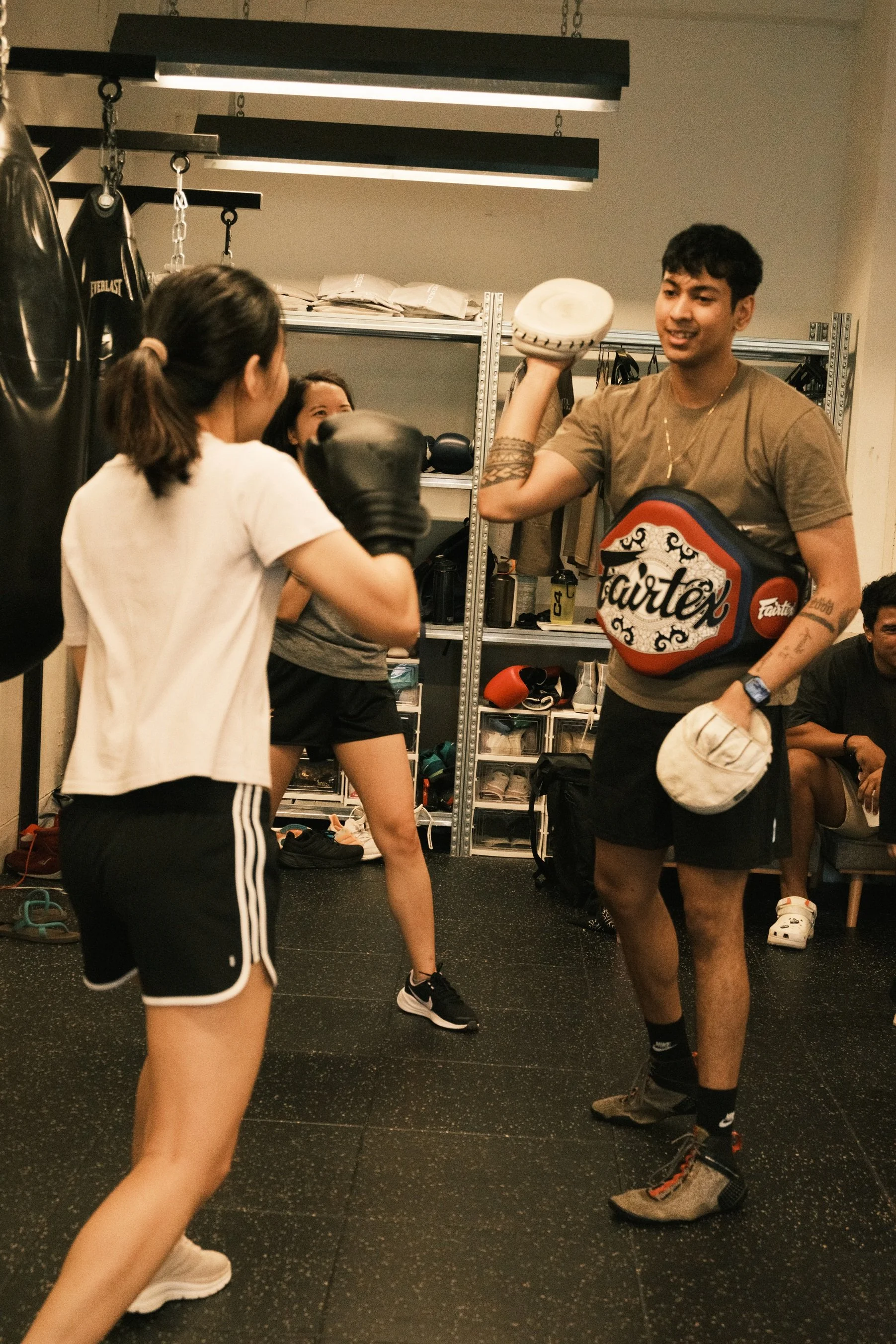 Boxing coach holding Fairtex Muay Thai pads while training two women at a Singapore boxing gym