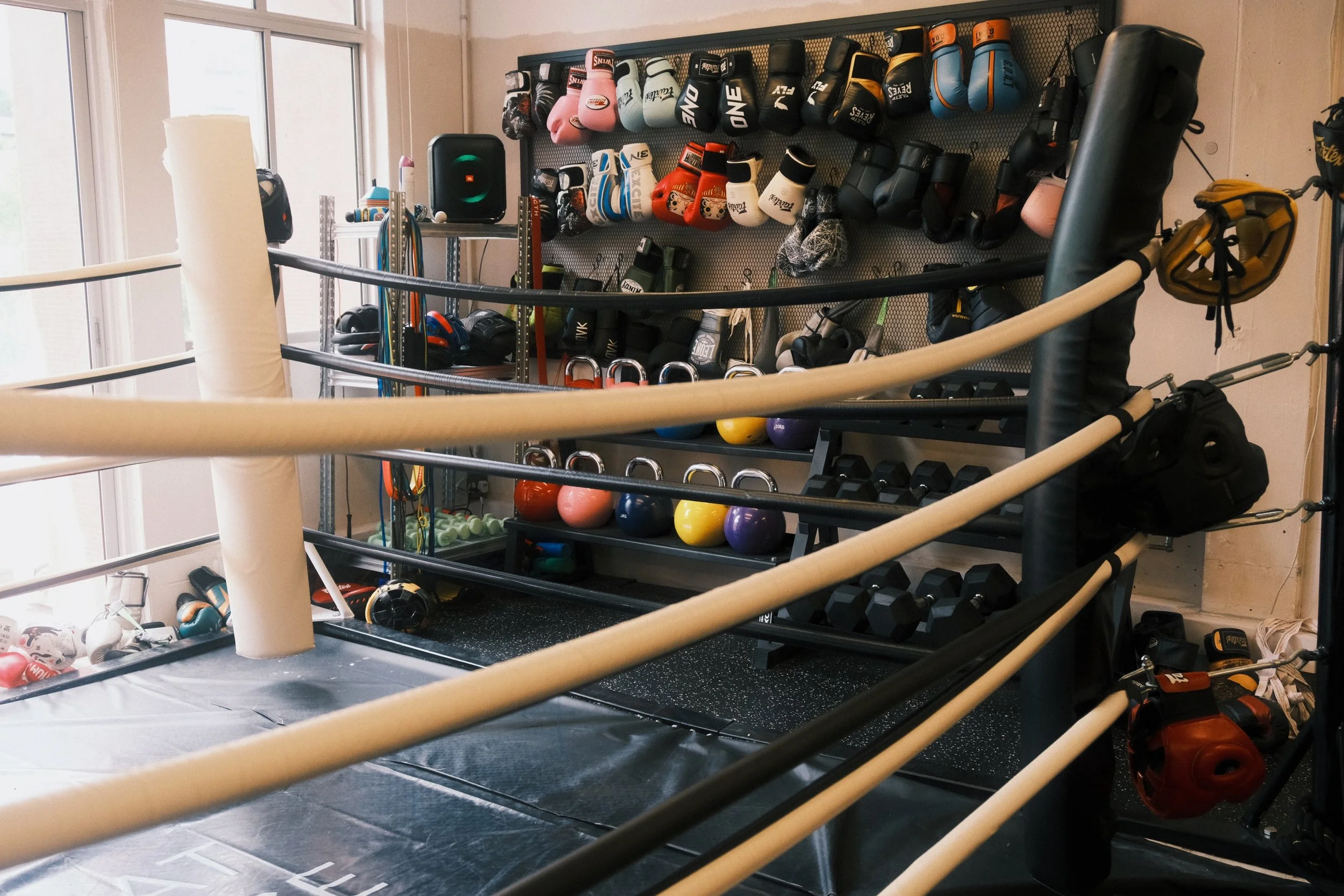 Boxing ring and equipment wall at Sweat Science Studio, boutique boxing gym in Singapore, featuring gloves, dumbbells, and kettlebells