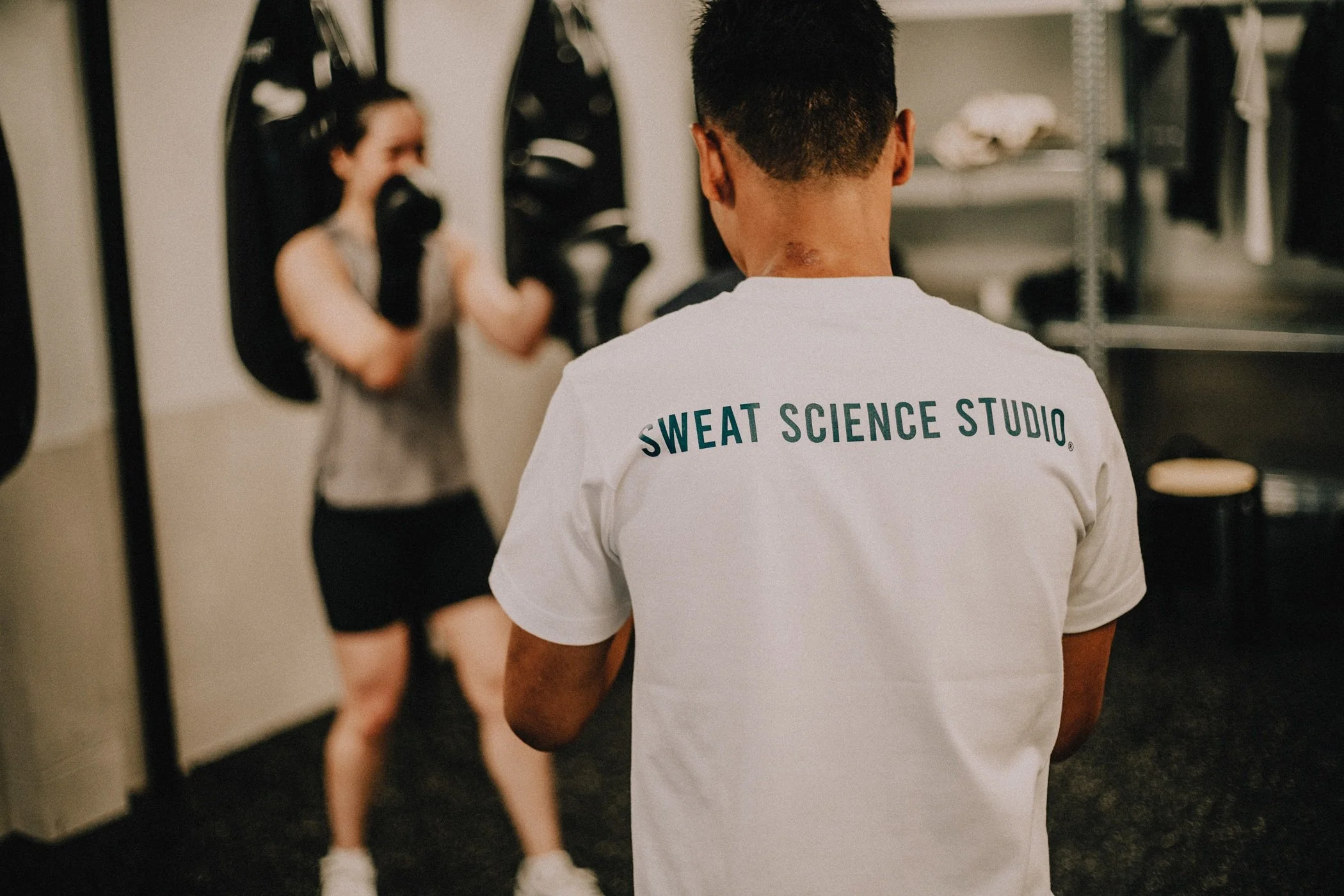 Boxing coach at Sweat Science Studio watching a member train on the heavy bag, Clarke Quay Singapore