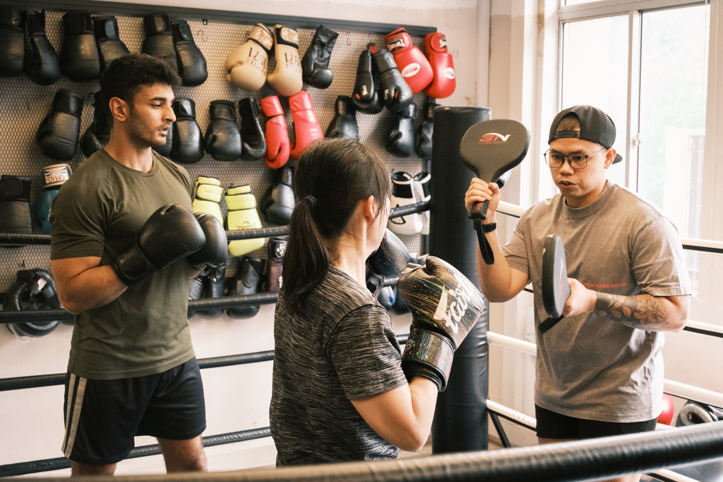 Boxing coach holding focus mitts for two members during pad work training at Sweat Science Studio, Clarke Quay