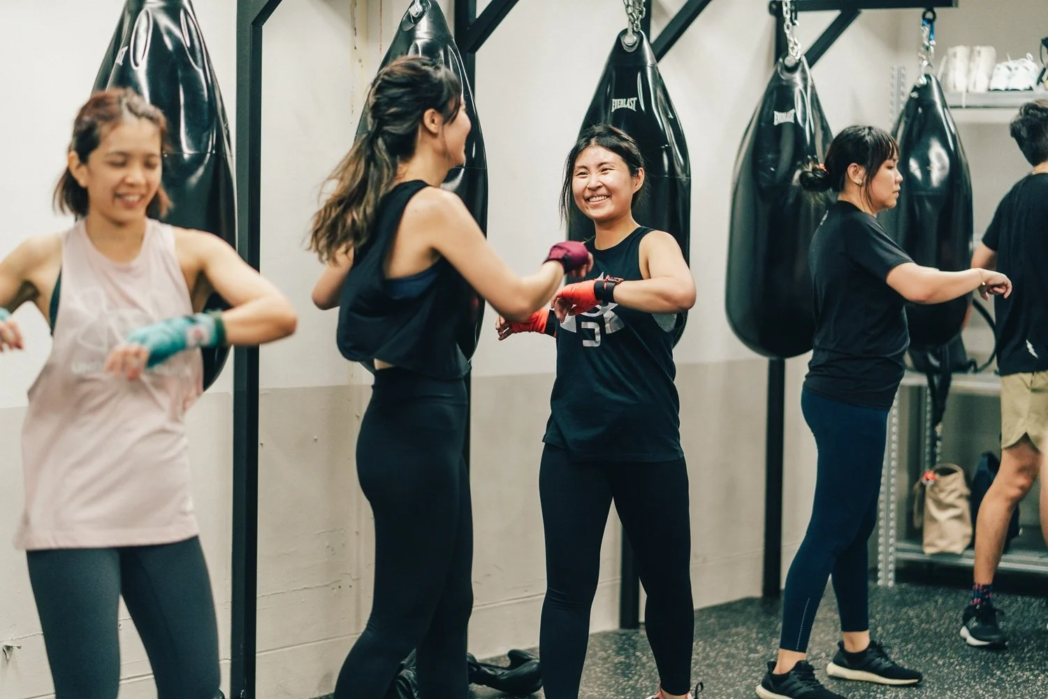 Women smiling during a boxing bag workout at Sweat Science Studio boutique boxing gym, Singapore CBD