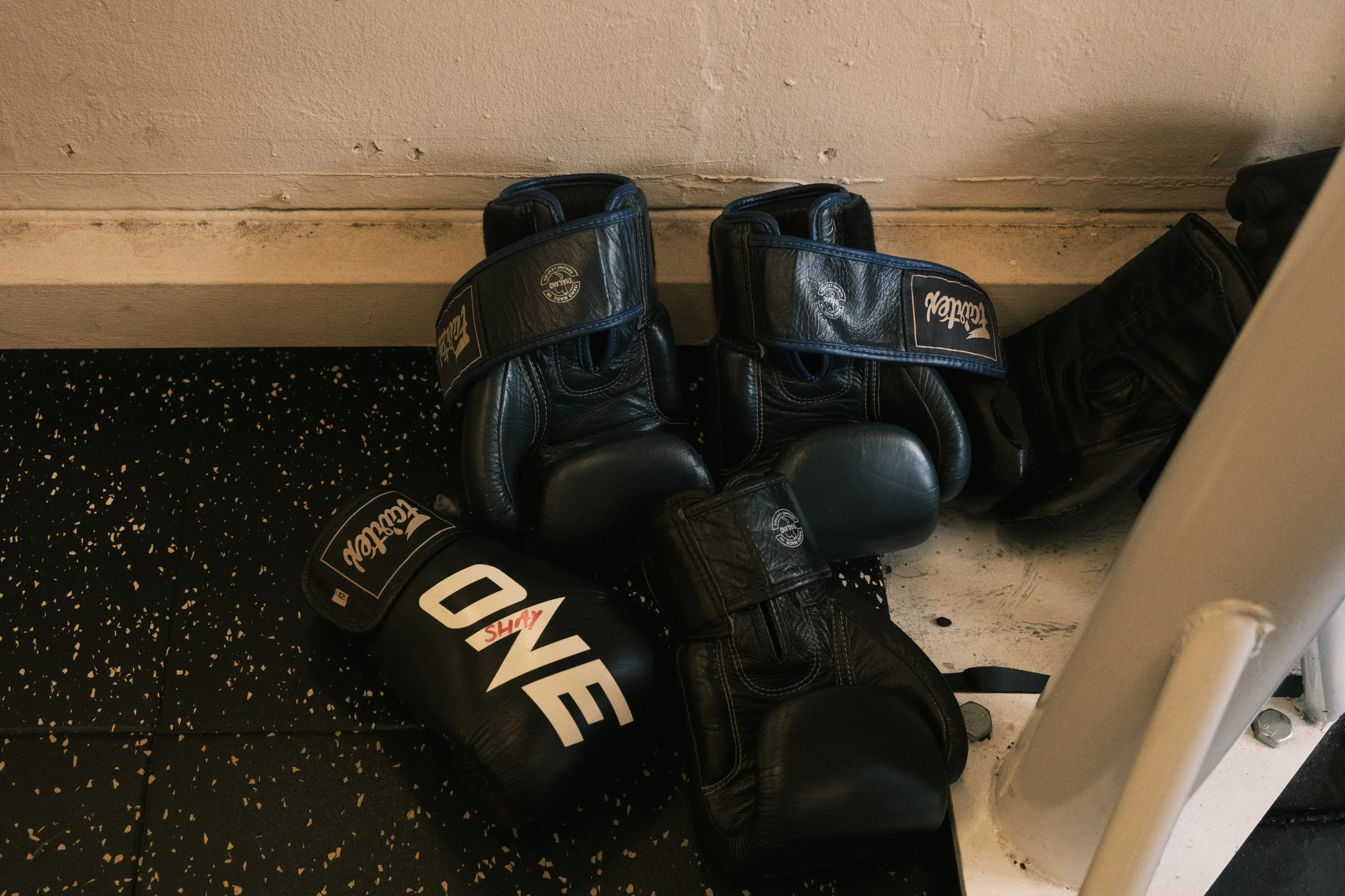 Worn leather Fairtex and Twins boxing gloves stacked on gym floor at Sweat Science Studio, Clarke Quay