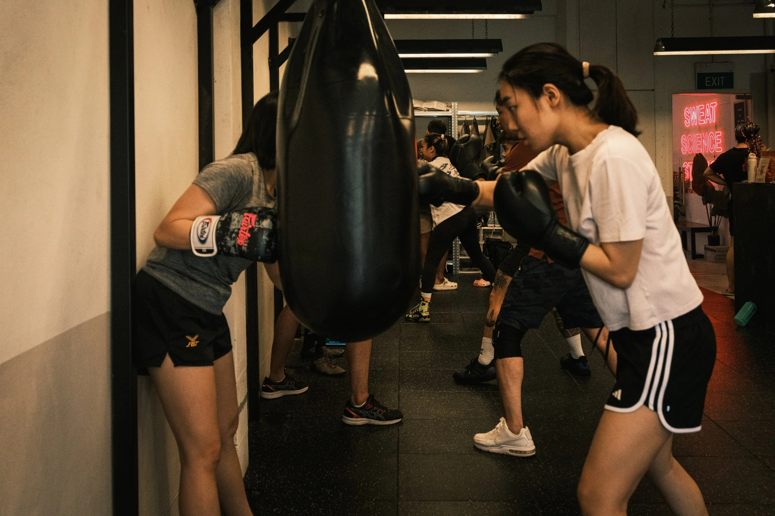 Women throwing jab-cross combinations on punching bags during a boxing class at Sweat Science Studio, Clarke Quay, Singapore