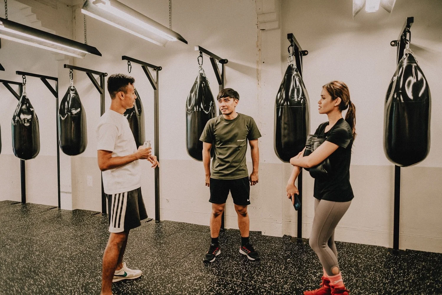 Boxing coach discussing technique with members between heavy bags at Sweat Science Studio Singapore