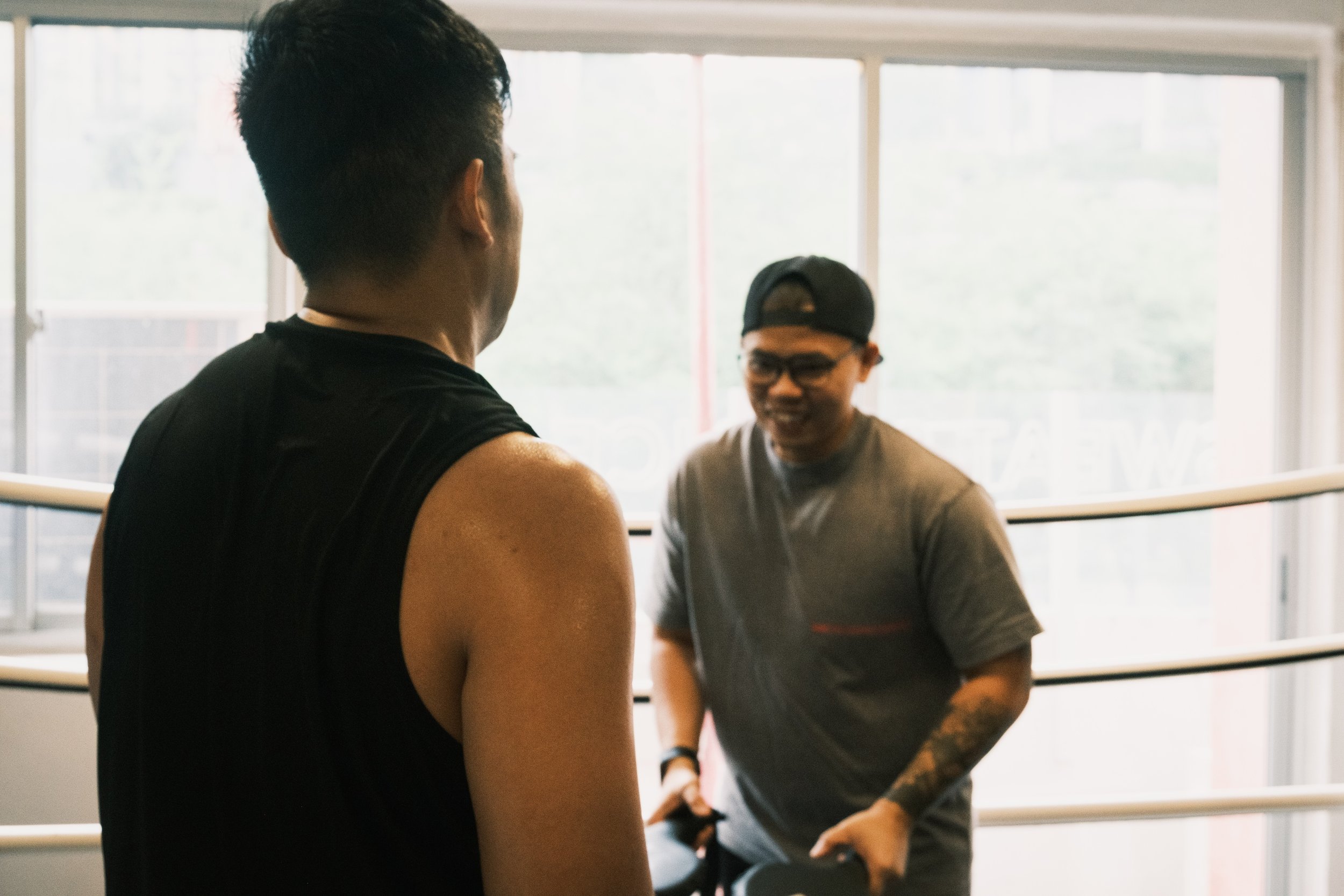 Boxing coach speaking with a member beside the ring at Sweat Science Studio boxing gym in Singapore